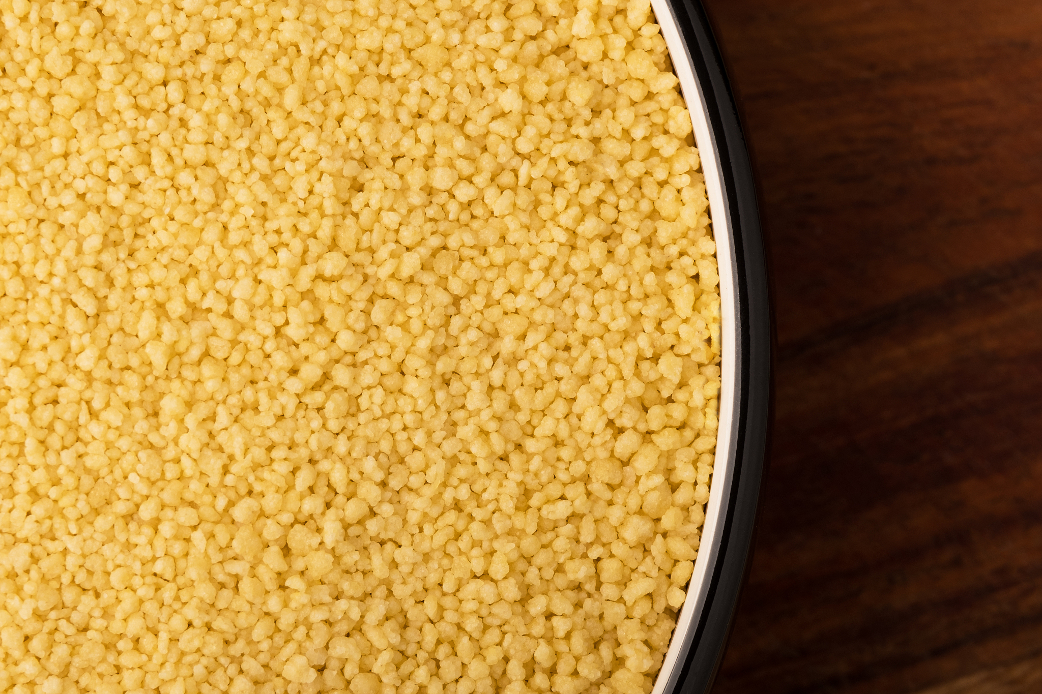 raw couscous in bowl on dark wooden background from above
