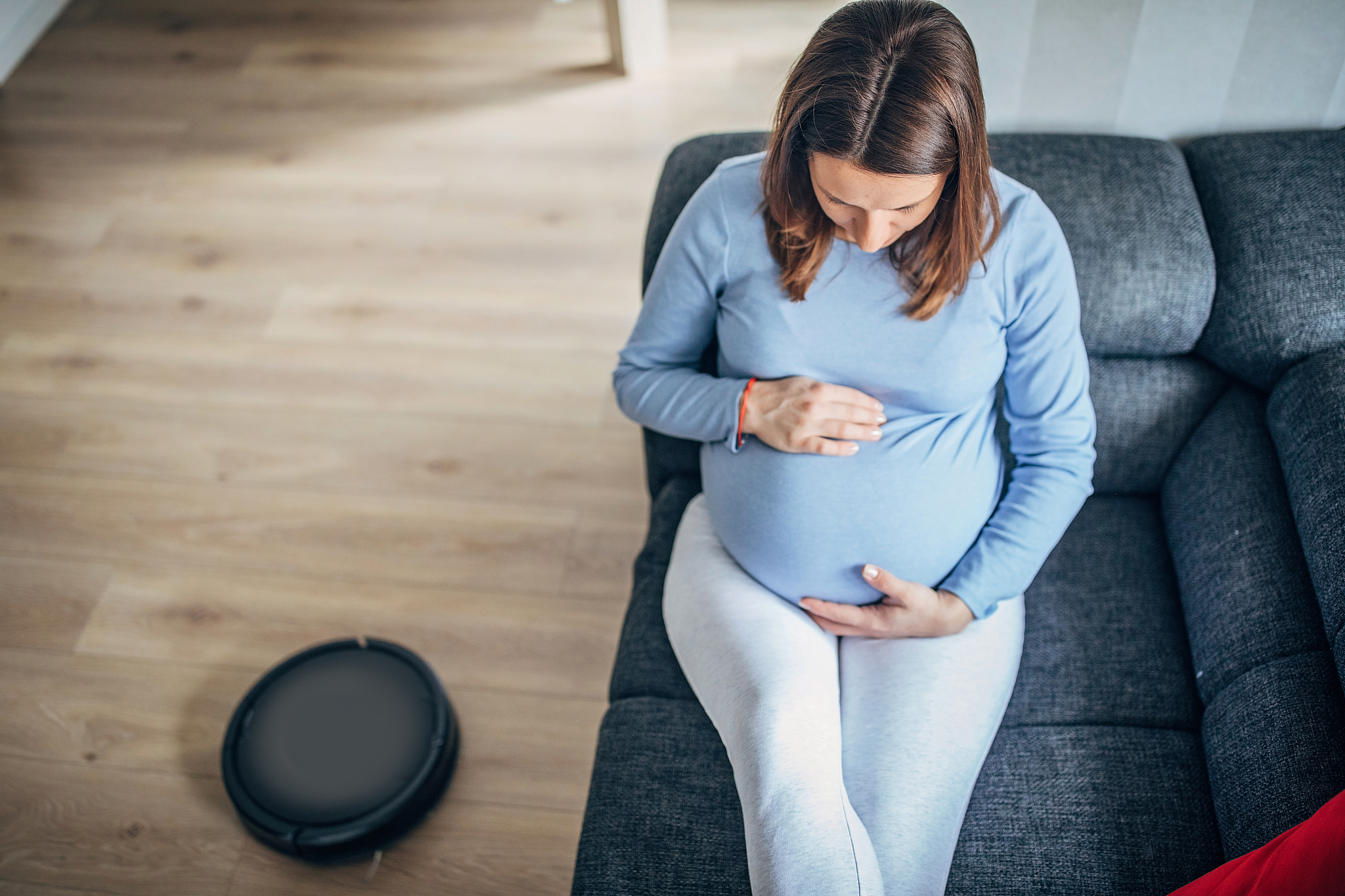 pregnant woman resting while robot vacuum cleaner cleaning floor