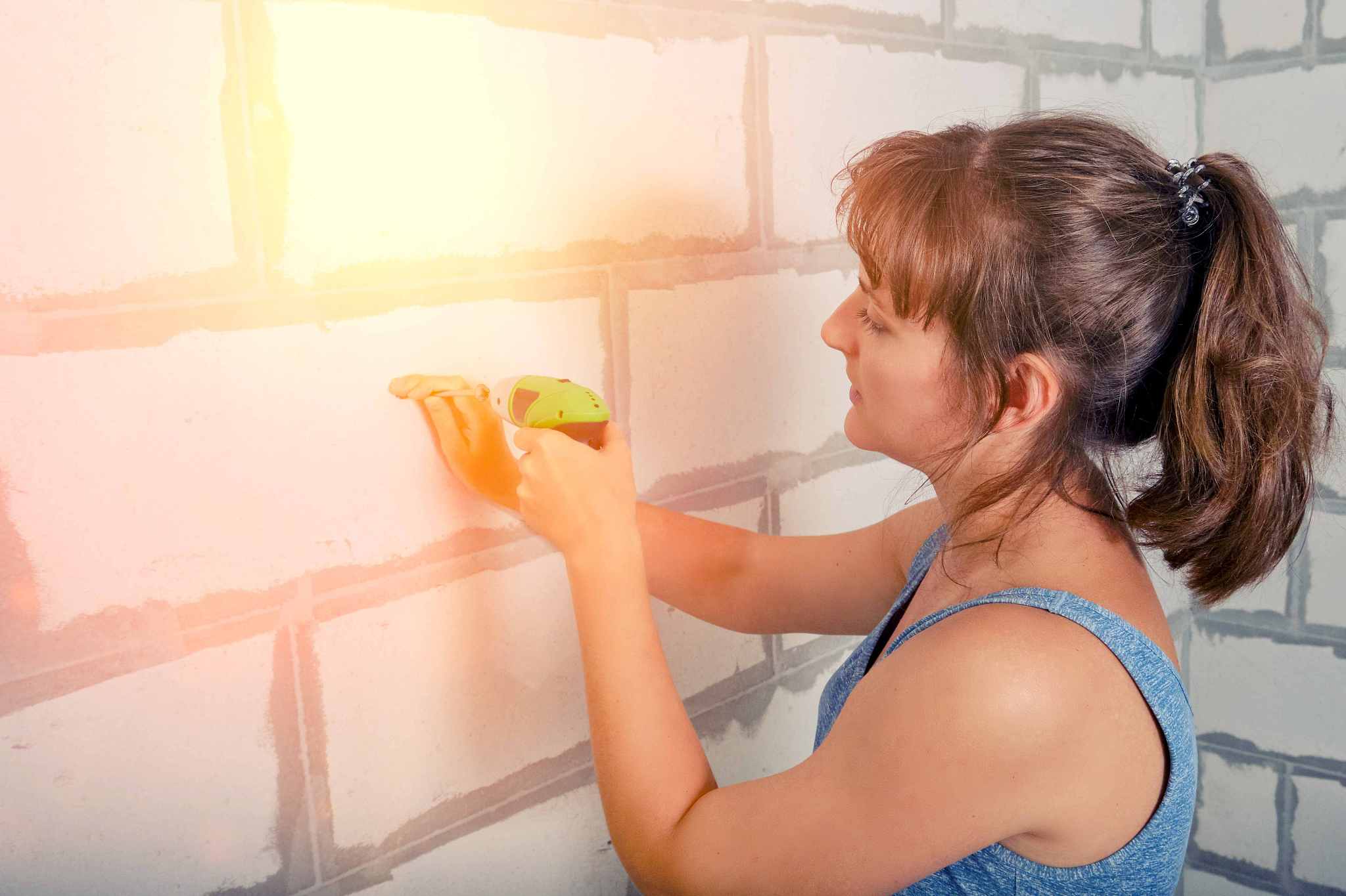 a woman drills a hole in the wall with a hand drill. screwing a 