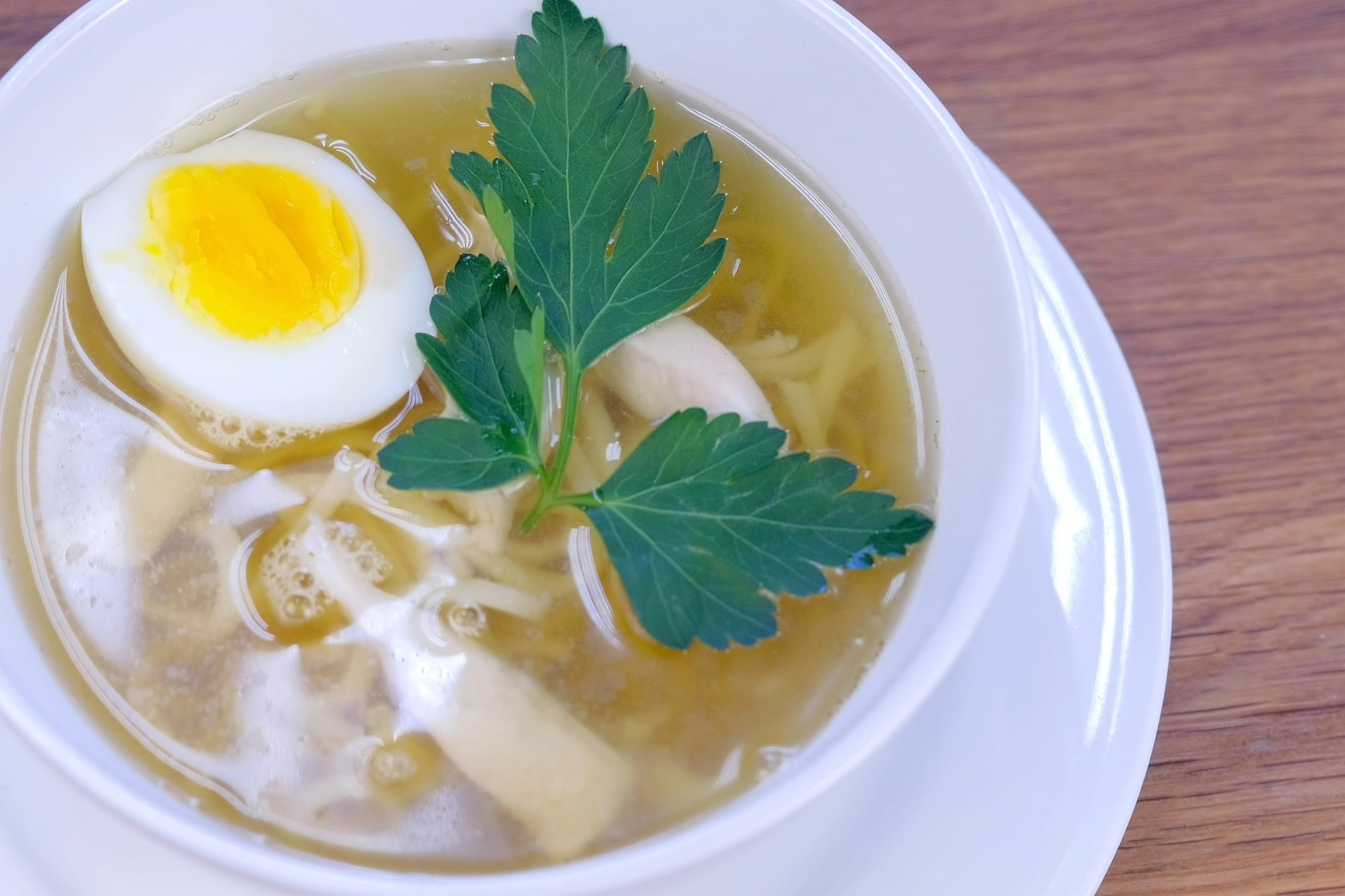 chicken soup with noodles, egg and greens in white bowl.