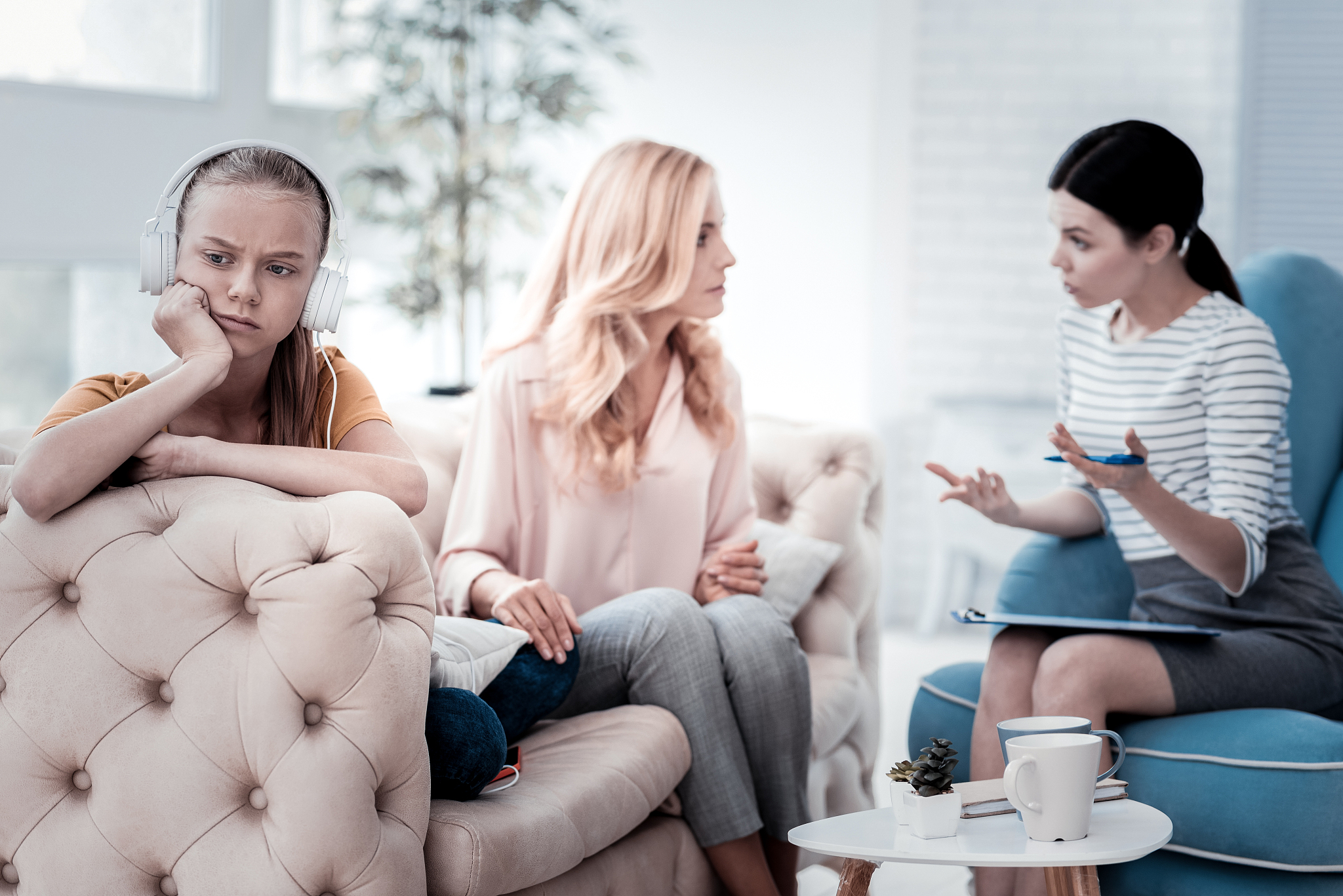 sad girl looking away while her mother talking with psychologist