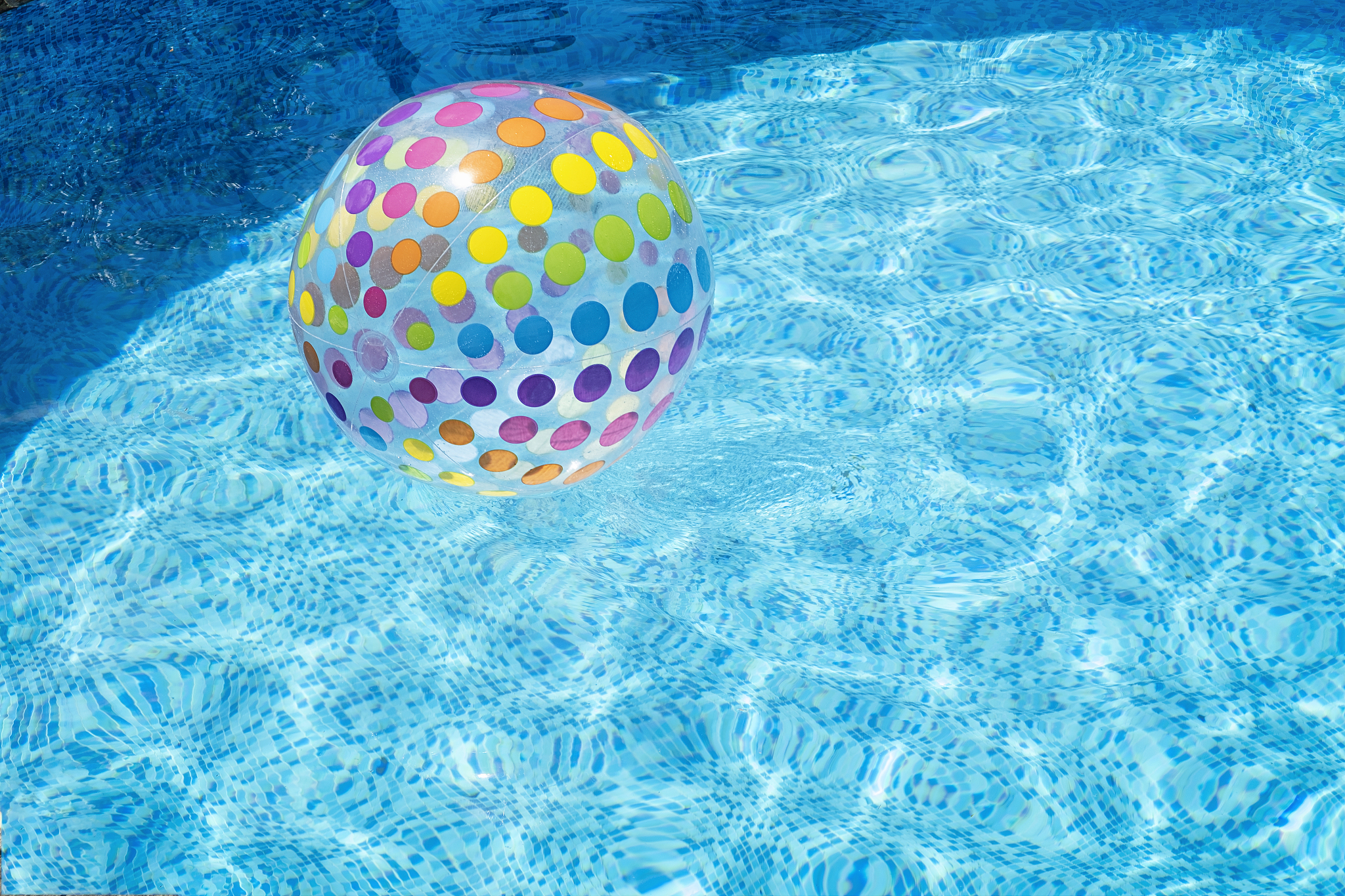 inflatable colourful ball floating in blue swimming pool water a