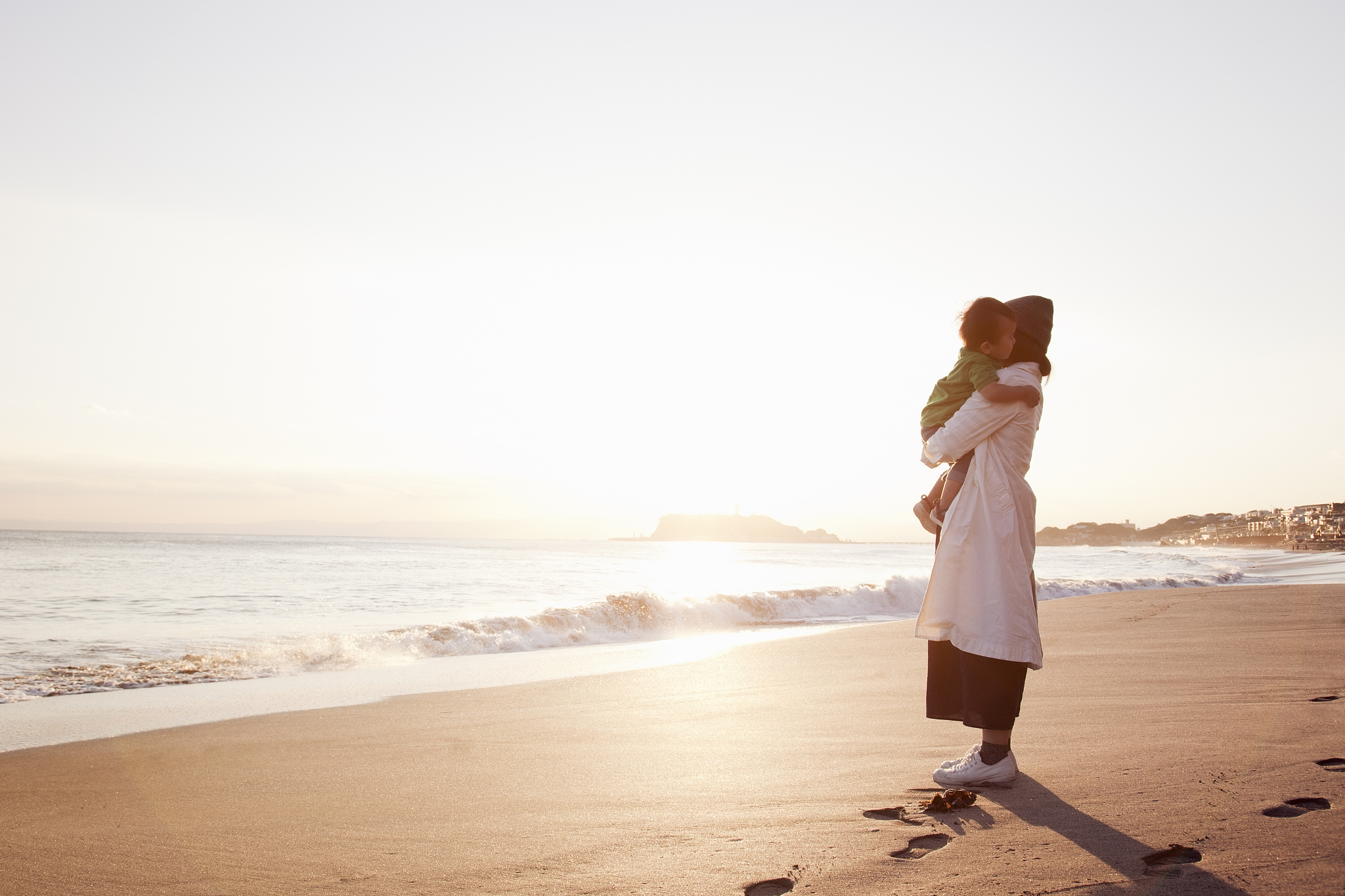 a mother and baby boy standing on the beach