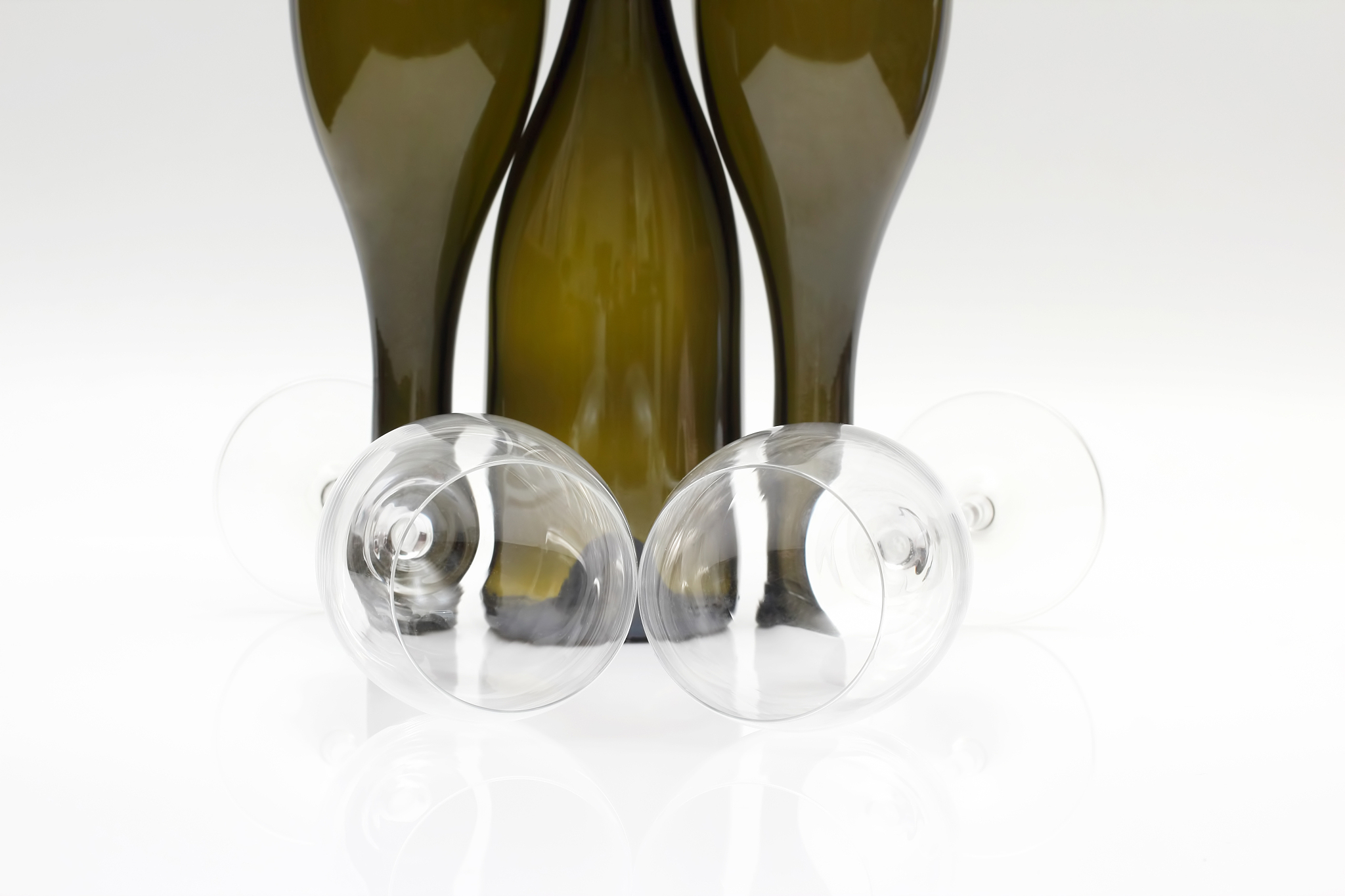 three empty wine bottles and two glasses close up on a white bac
