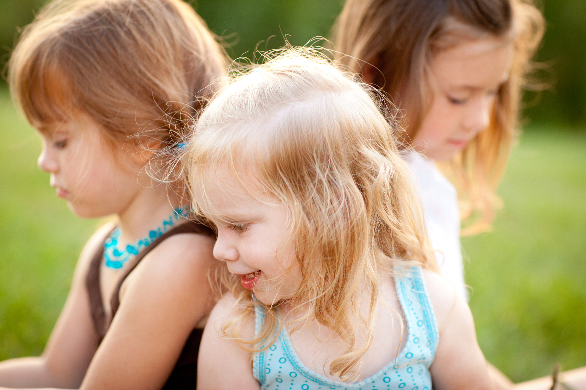 three happy little sisters sitting together outside