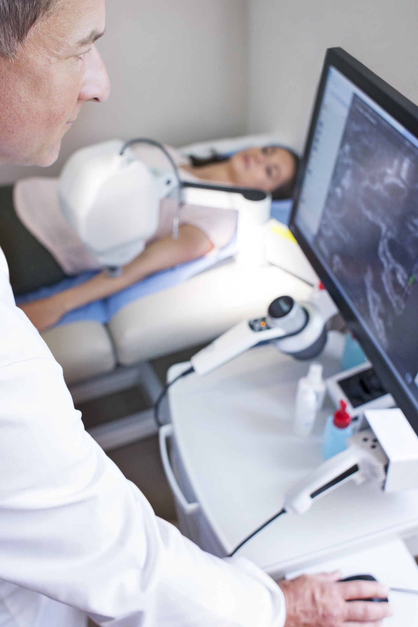 doctor looking at computer monitor, patient on bed
