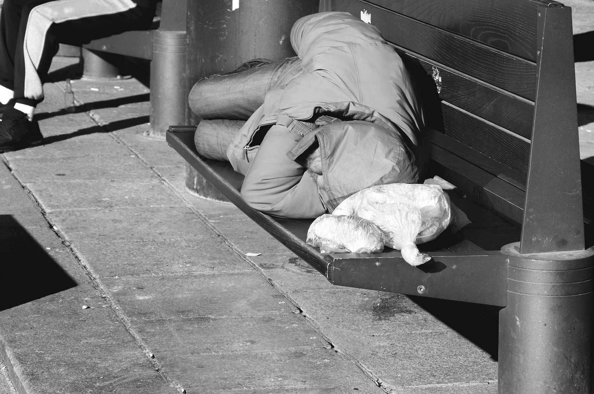 poor homeless man sleeps on the wooden bench at the street in th