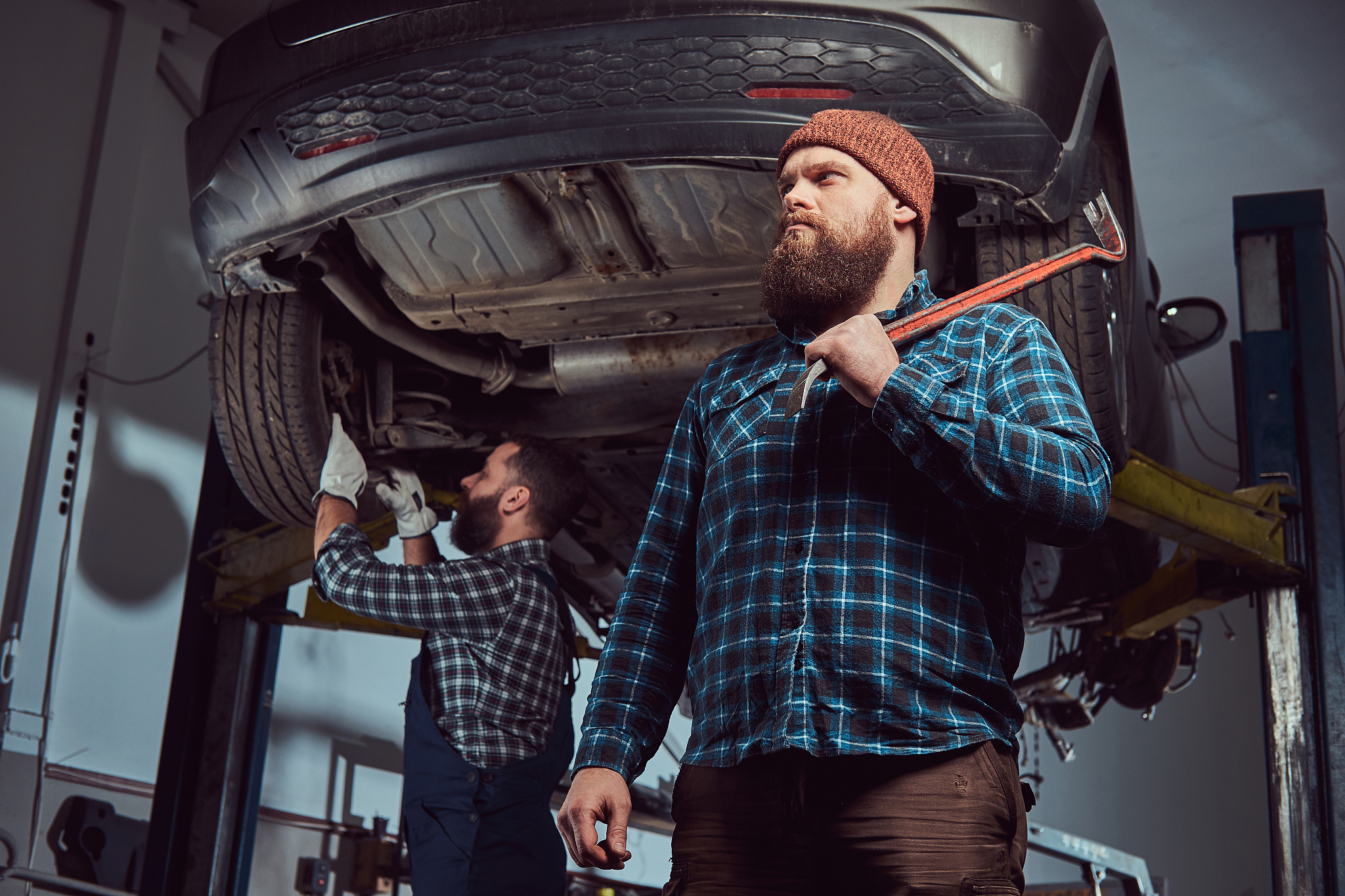 two bearded brutal mechanics repair a car on a lift in the garag