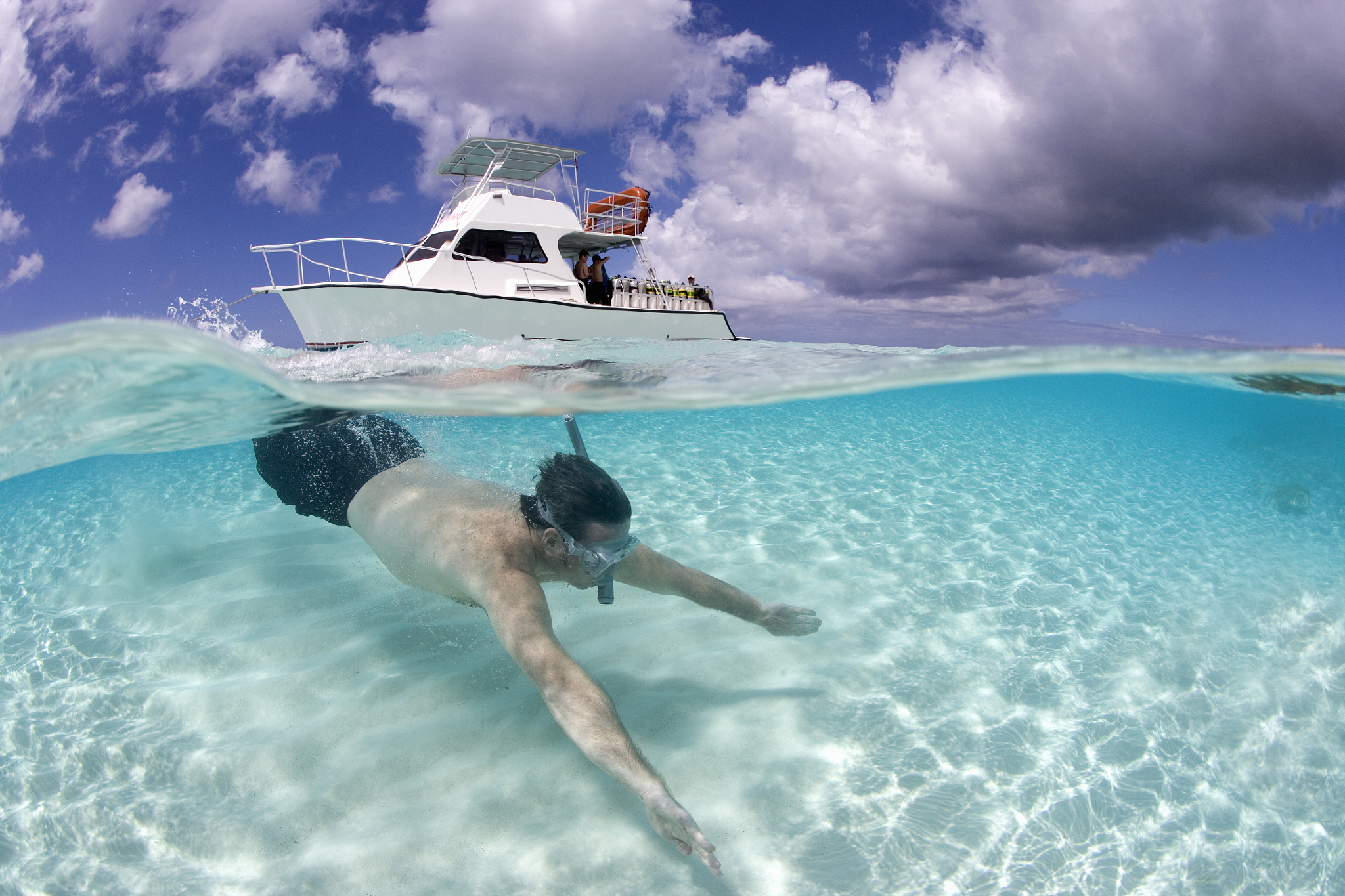 man snorkeling, dive boat in background, surface view