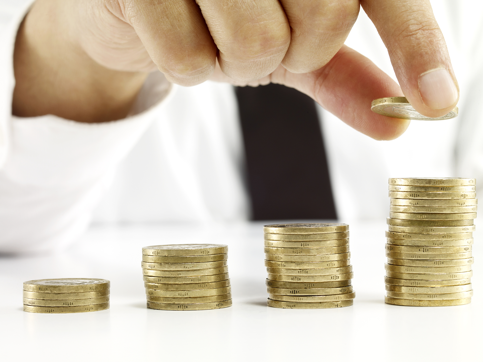 businessman's hand placing more coins on the highest stack