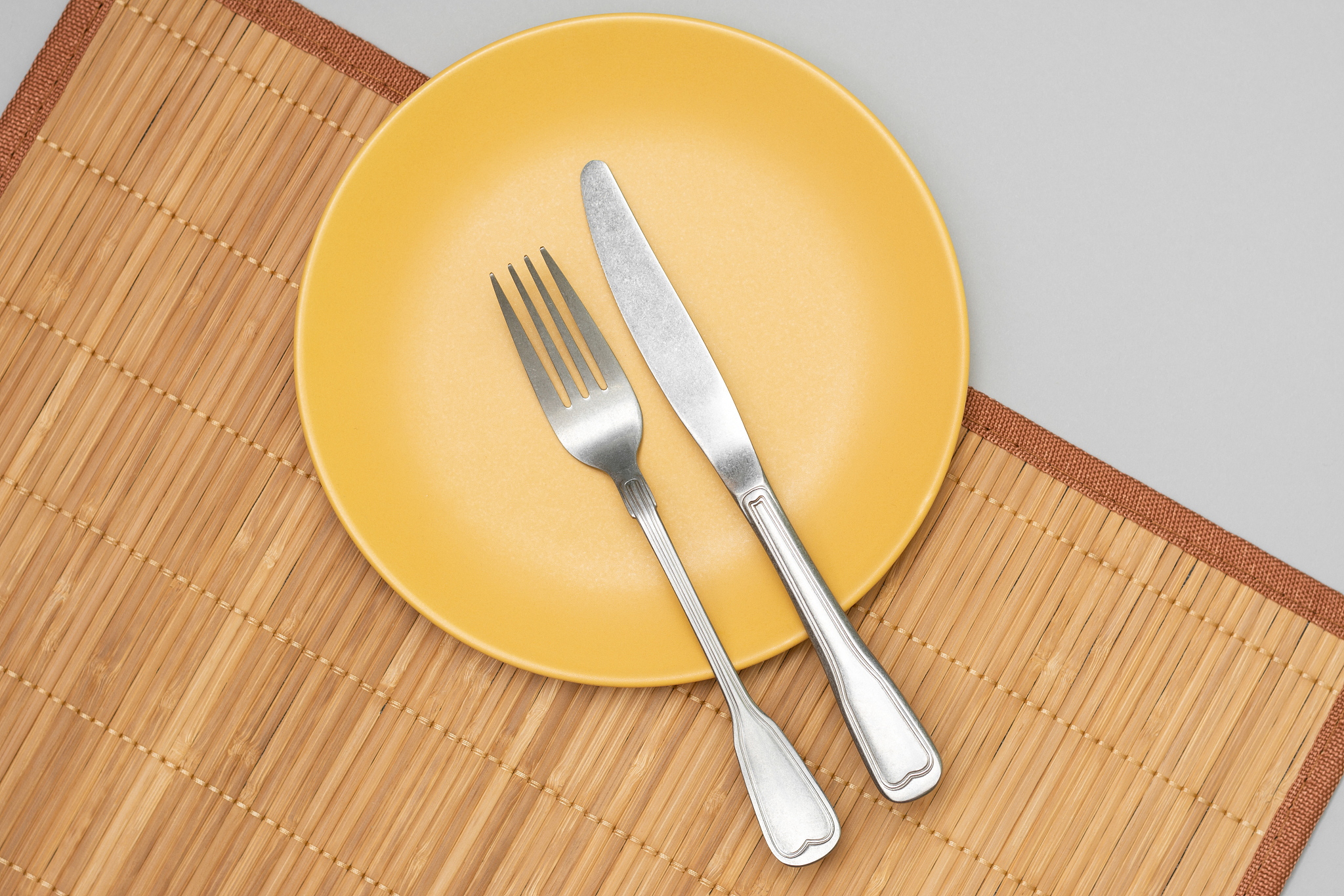 a yellow plate with a fork and knife on a mat on a gray backgrou