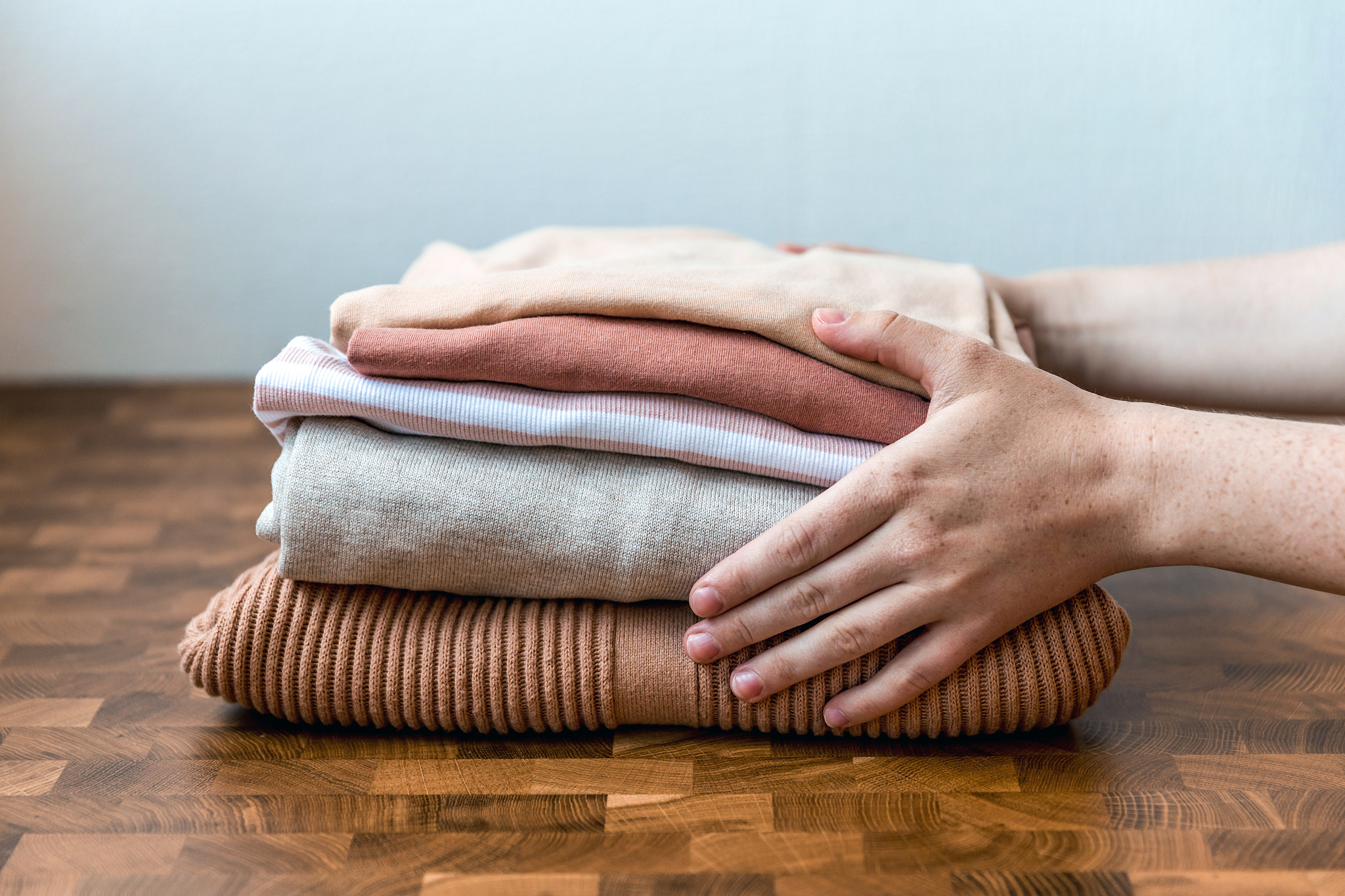 stack of beige tones clothes on the wooden table in the woman ha