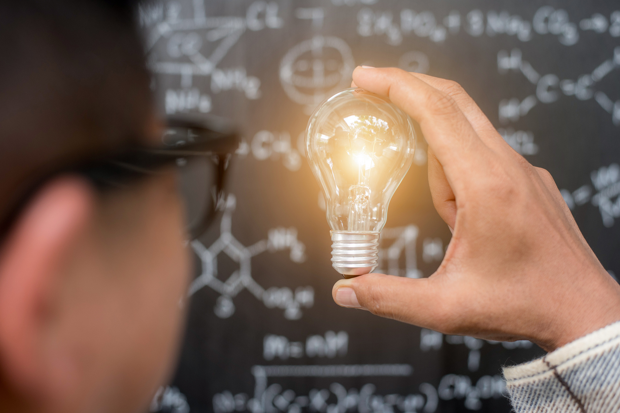 hand holding light bulb on blackboard background