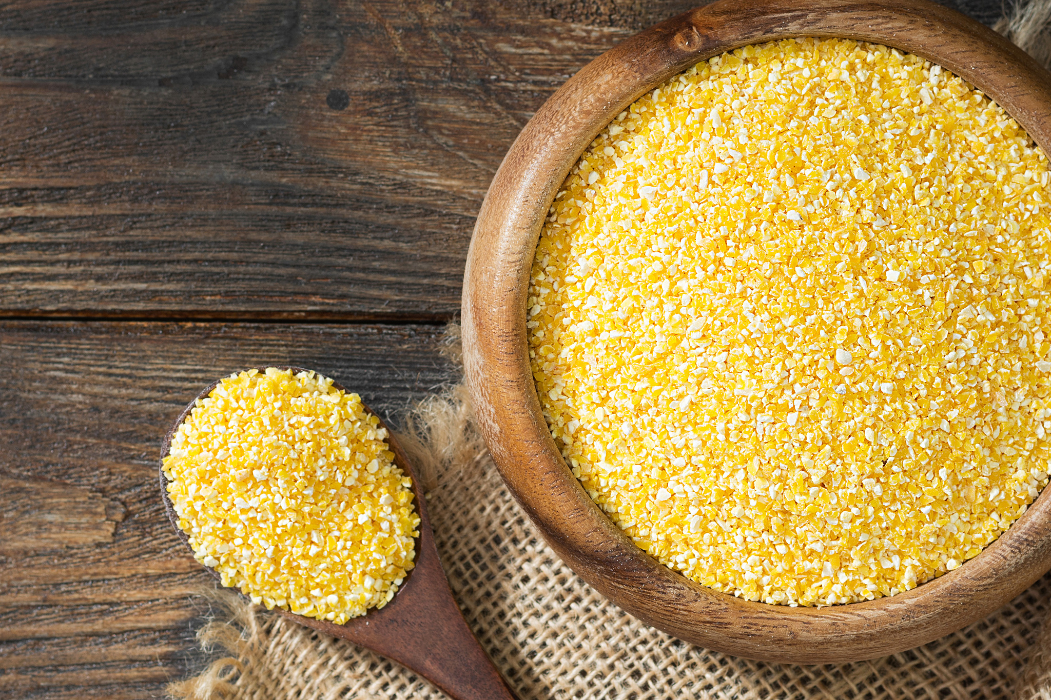 raw corn grits in a wooden bowl and wooden spoon on a wooden tab