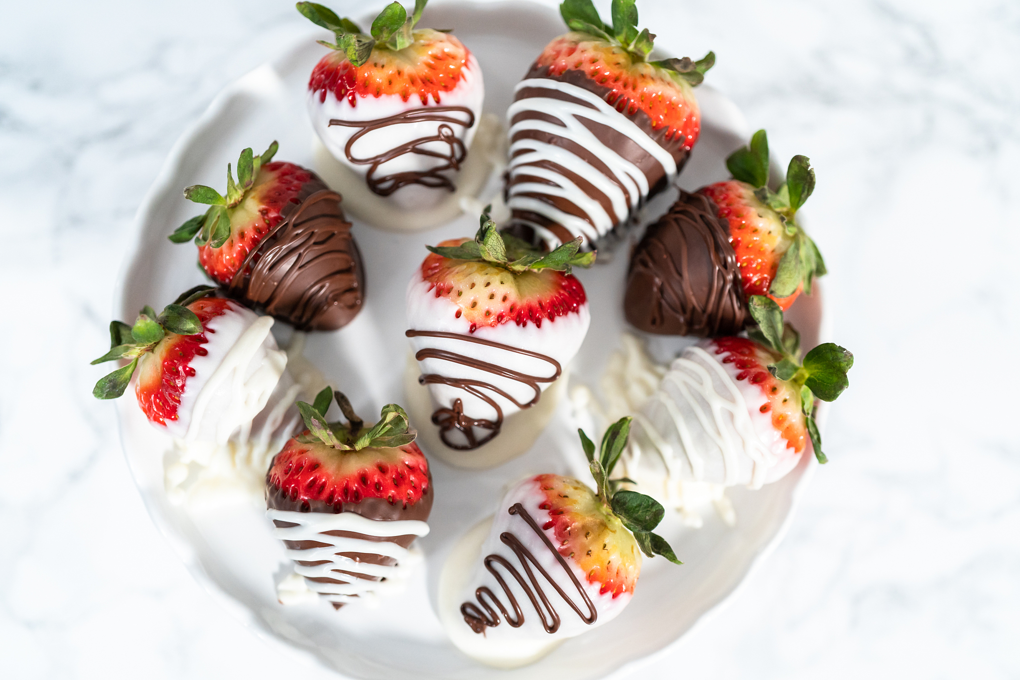 white and dark chocolate dipped strawberries on a white cake sta