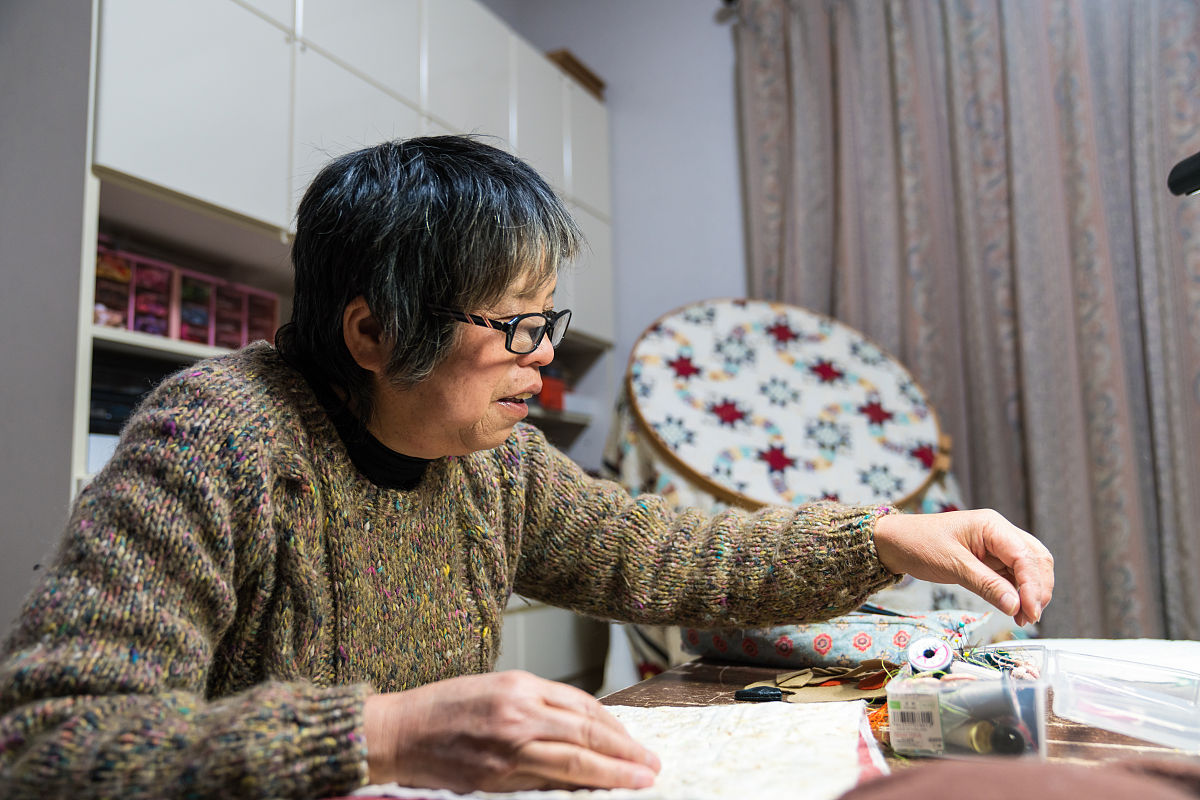 一位年长妇女在她的家中缝纫和制作工艺品