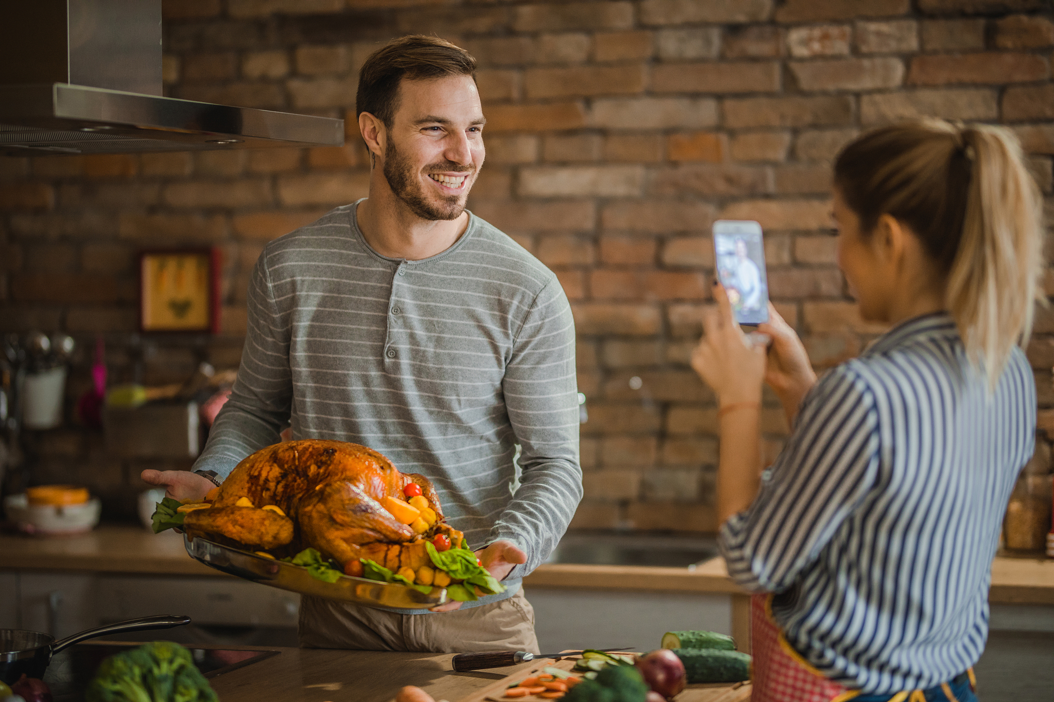 happy man being photographed with thanksgiving turkey by his gir