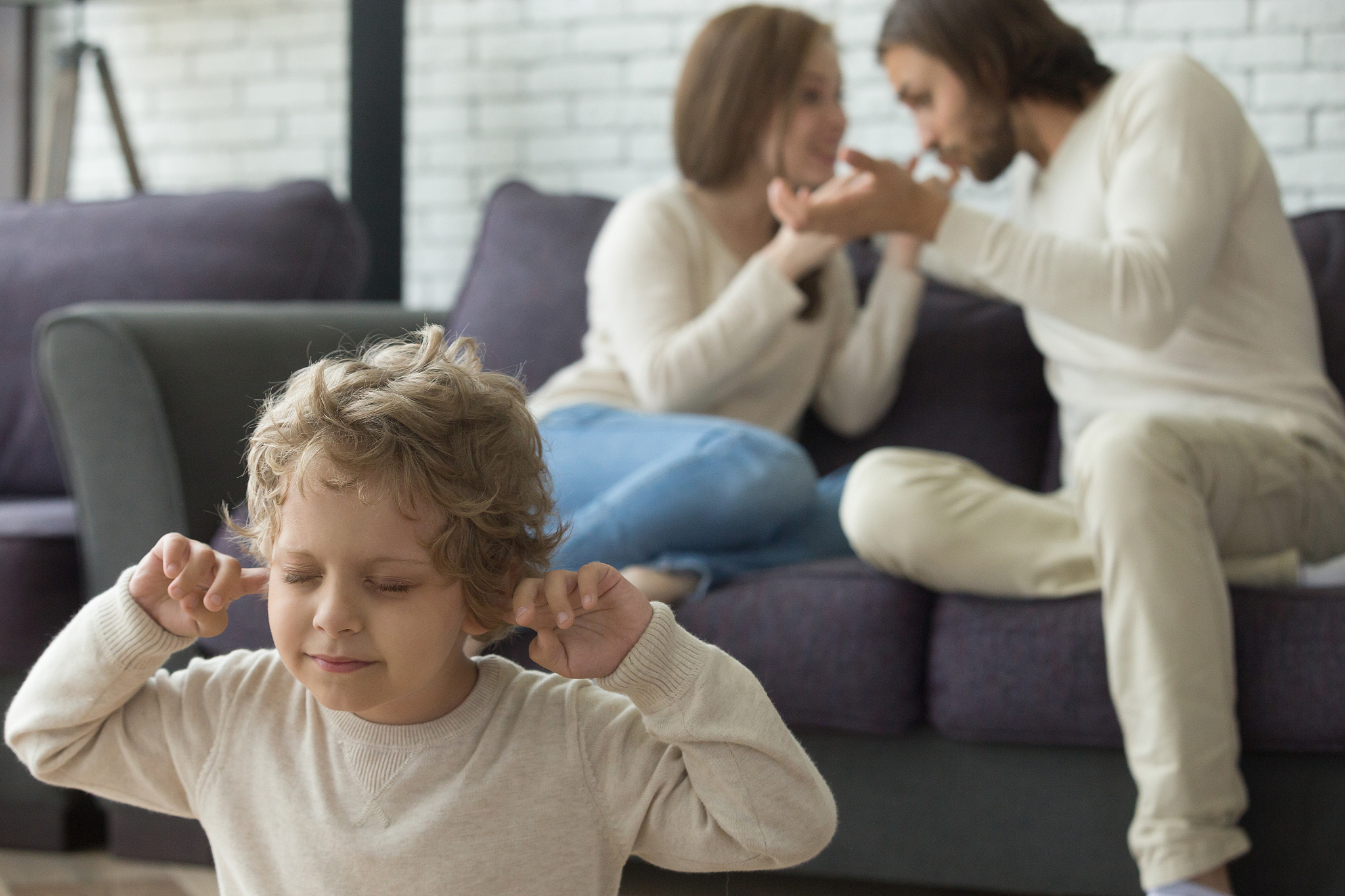 upset child son puts fingers in ears while parents fighting