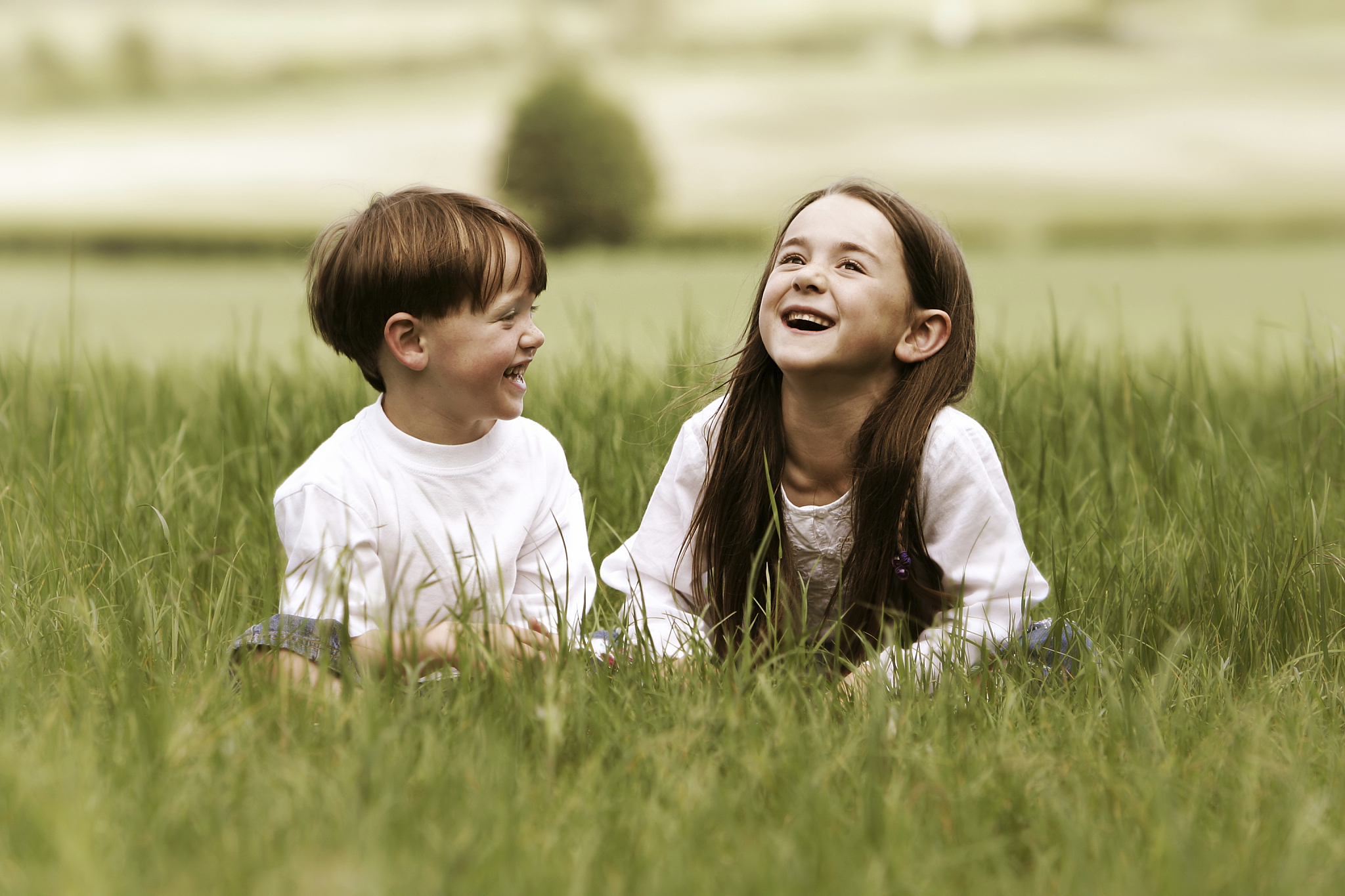 two young children sitting in grass and laughing