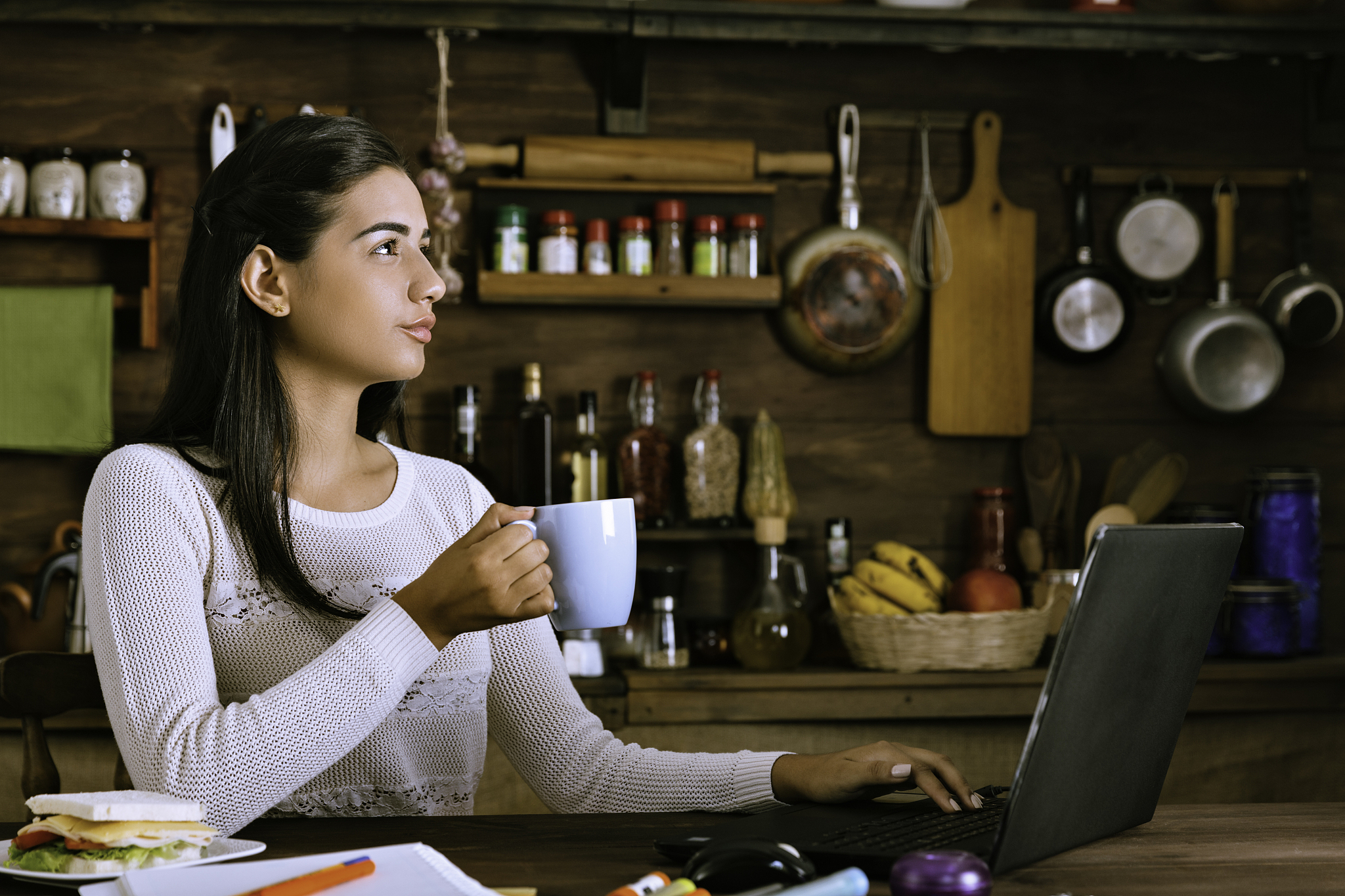 pensive hispanic young woman working in the kitchen and using la