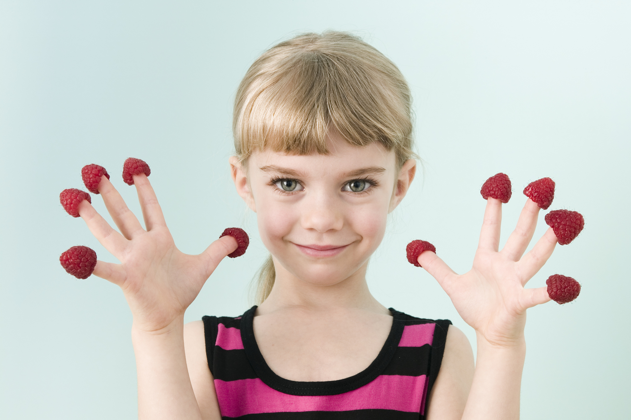 girl (3-5) with raspberries on fingers, smiling