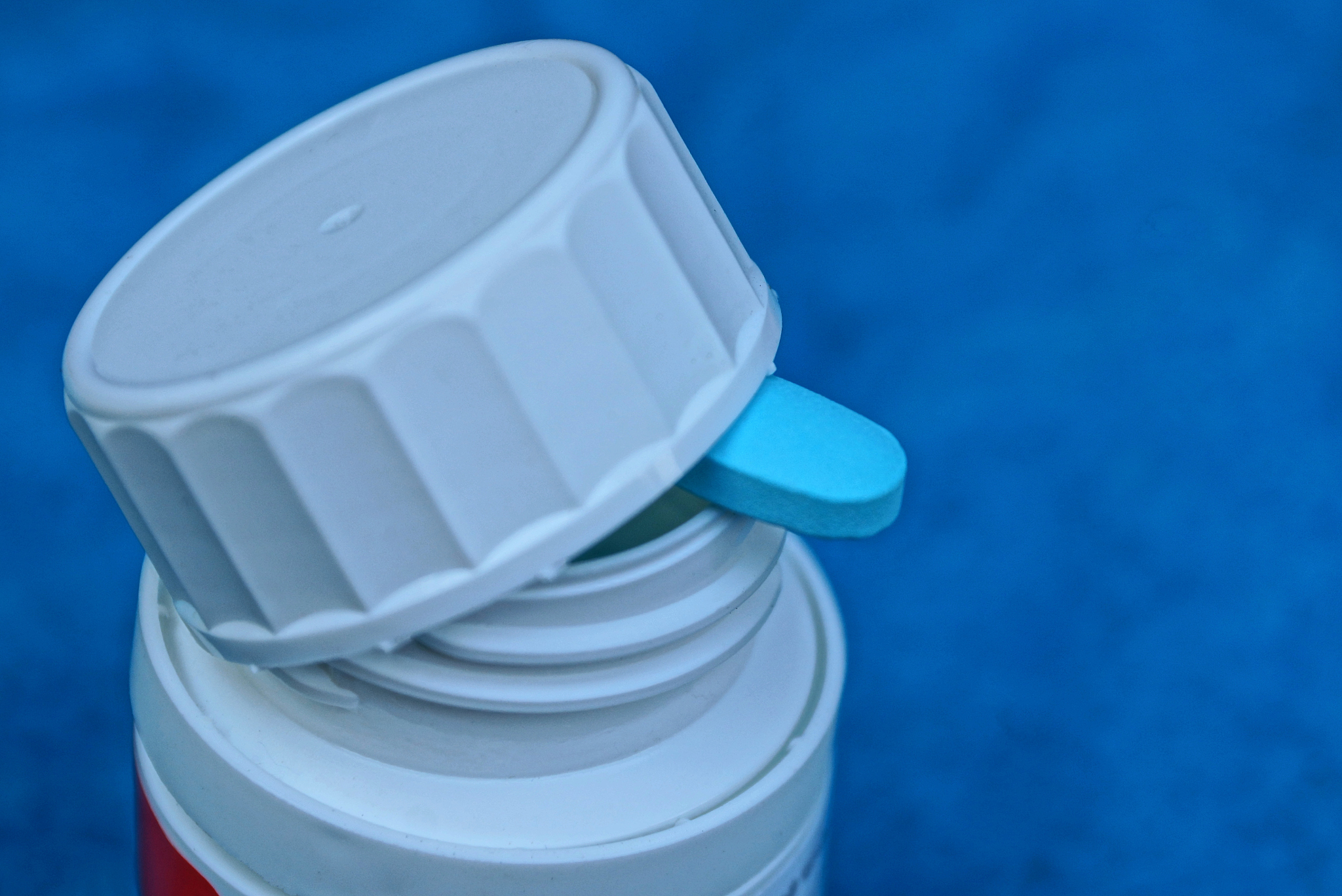 white plastic bottle and one blue tablet under the lid