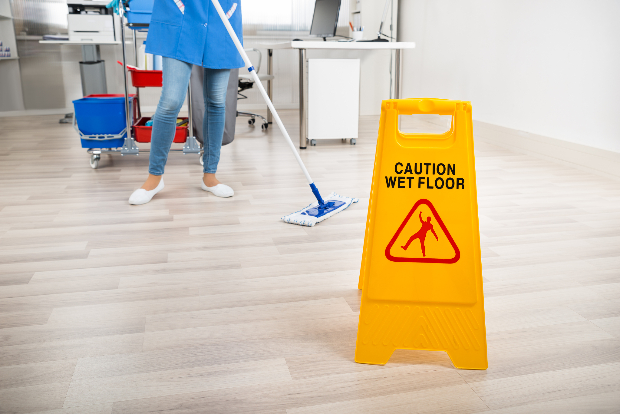 janitor mopping floor by wet caution sign in office