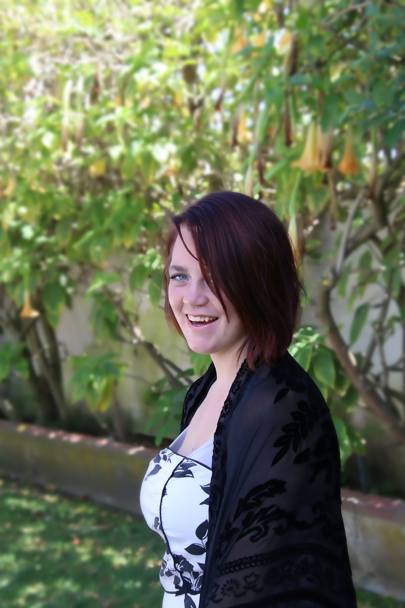 a pretty teenage girl is standing in a garden smiling.