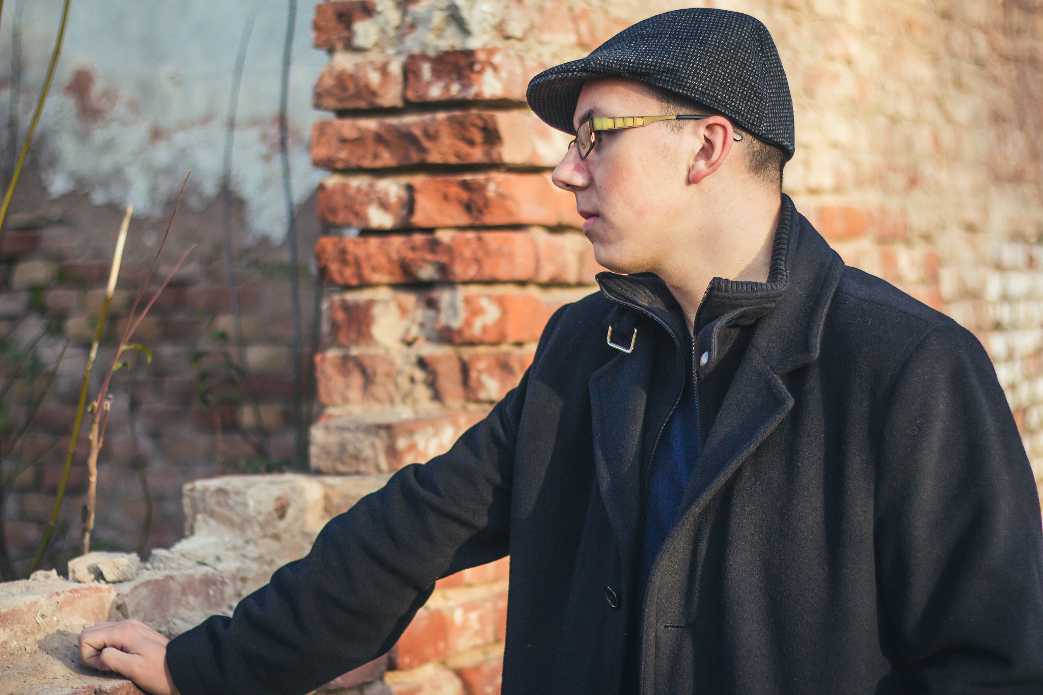 young teenage man next to brick wall.
