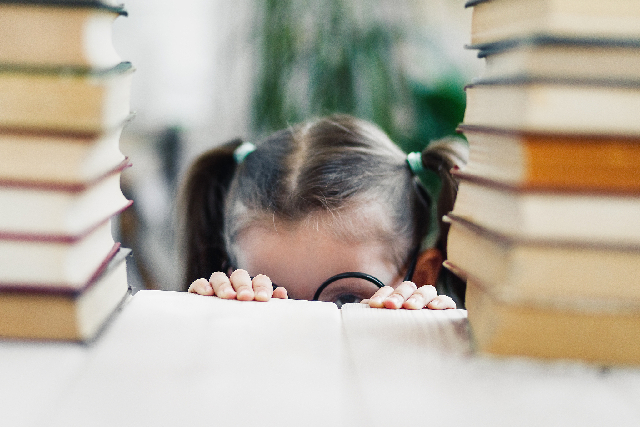 little child try to hide under a table from reading a pile of bo