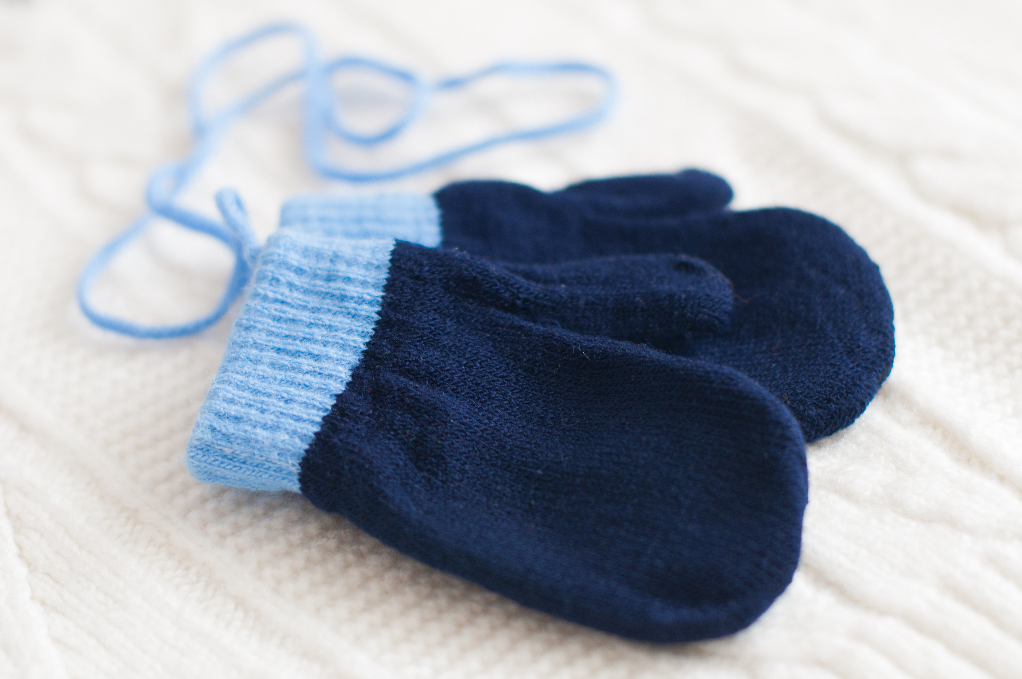 pair of blue knitted mittens on a white woolen fabric.