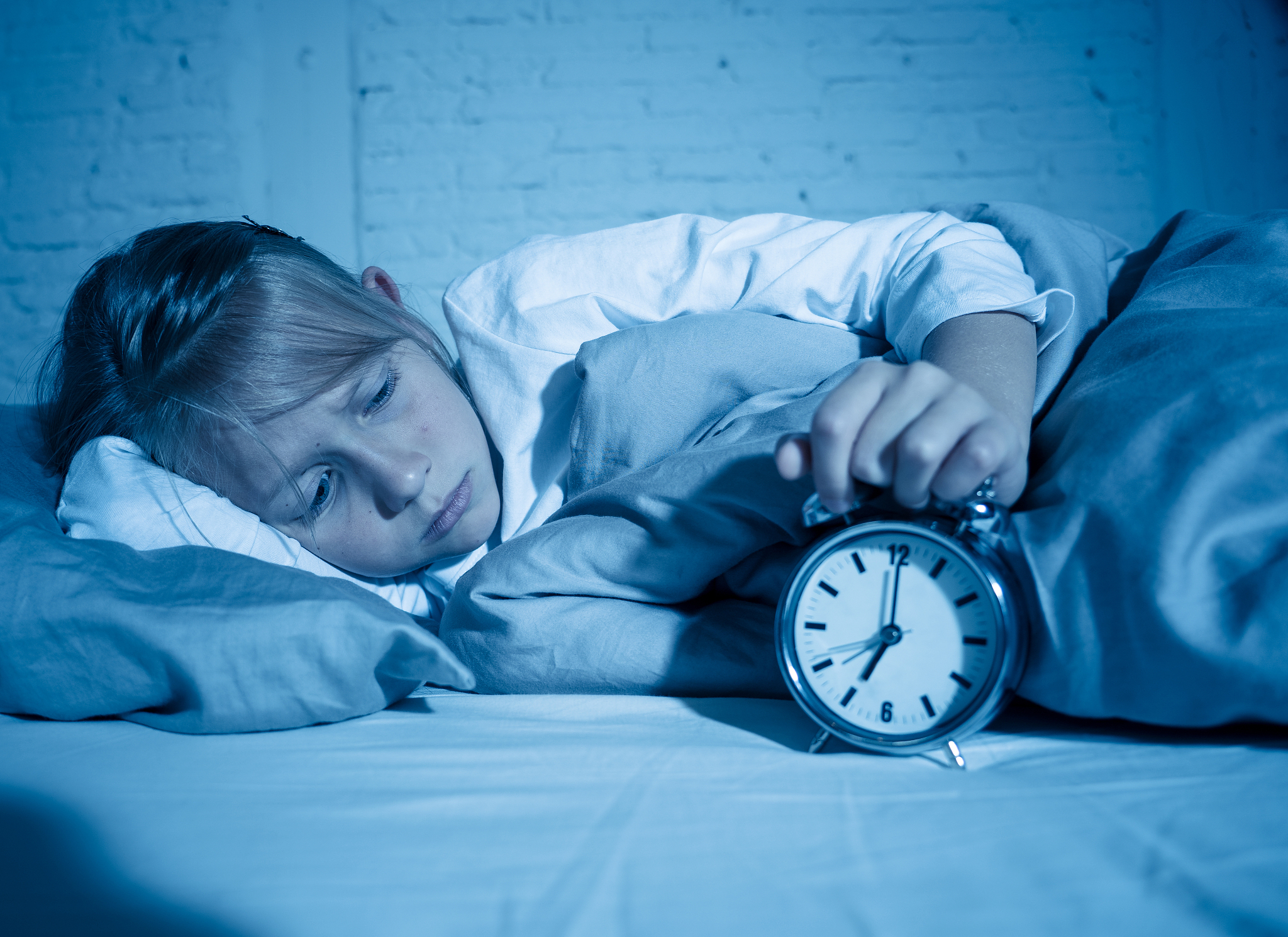 sweet sleepless little girl lying sad in bed looking at alarm cl