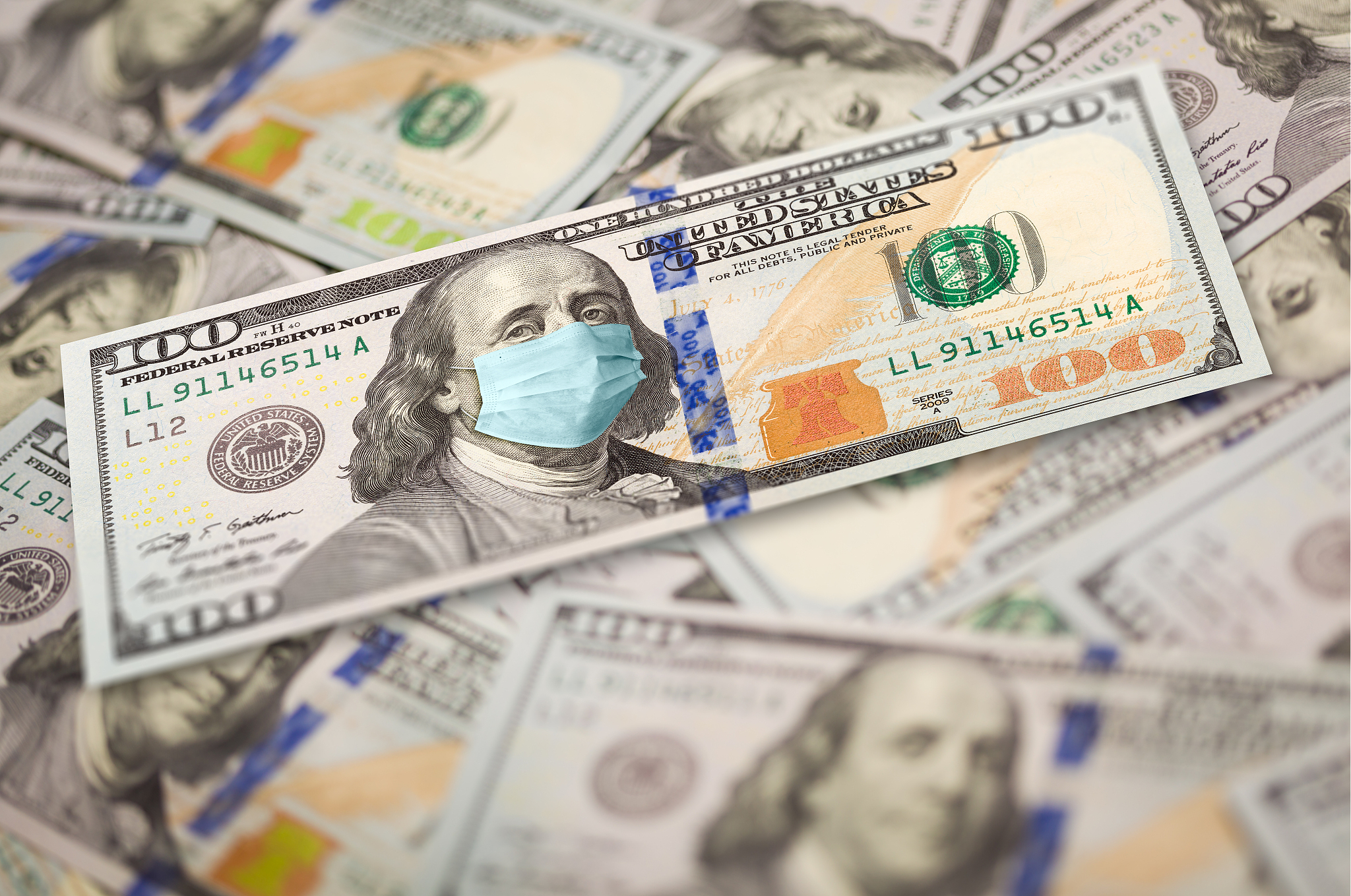 pile of one hundred dollar bills with medical face mask on face 