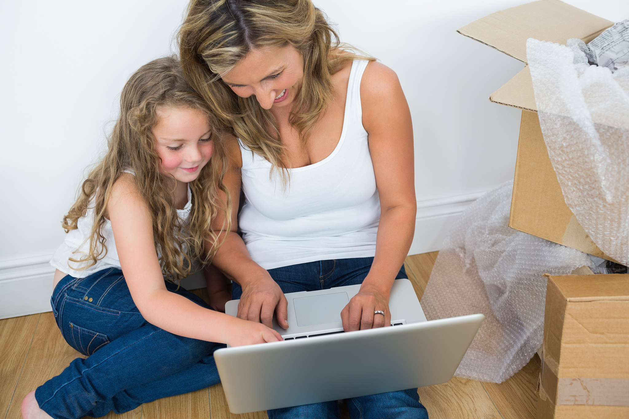 smiling mother and daughter using laptop while sitting on the fl