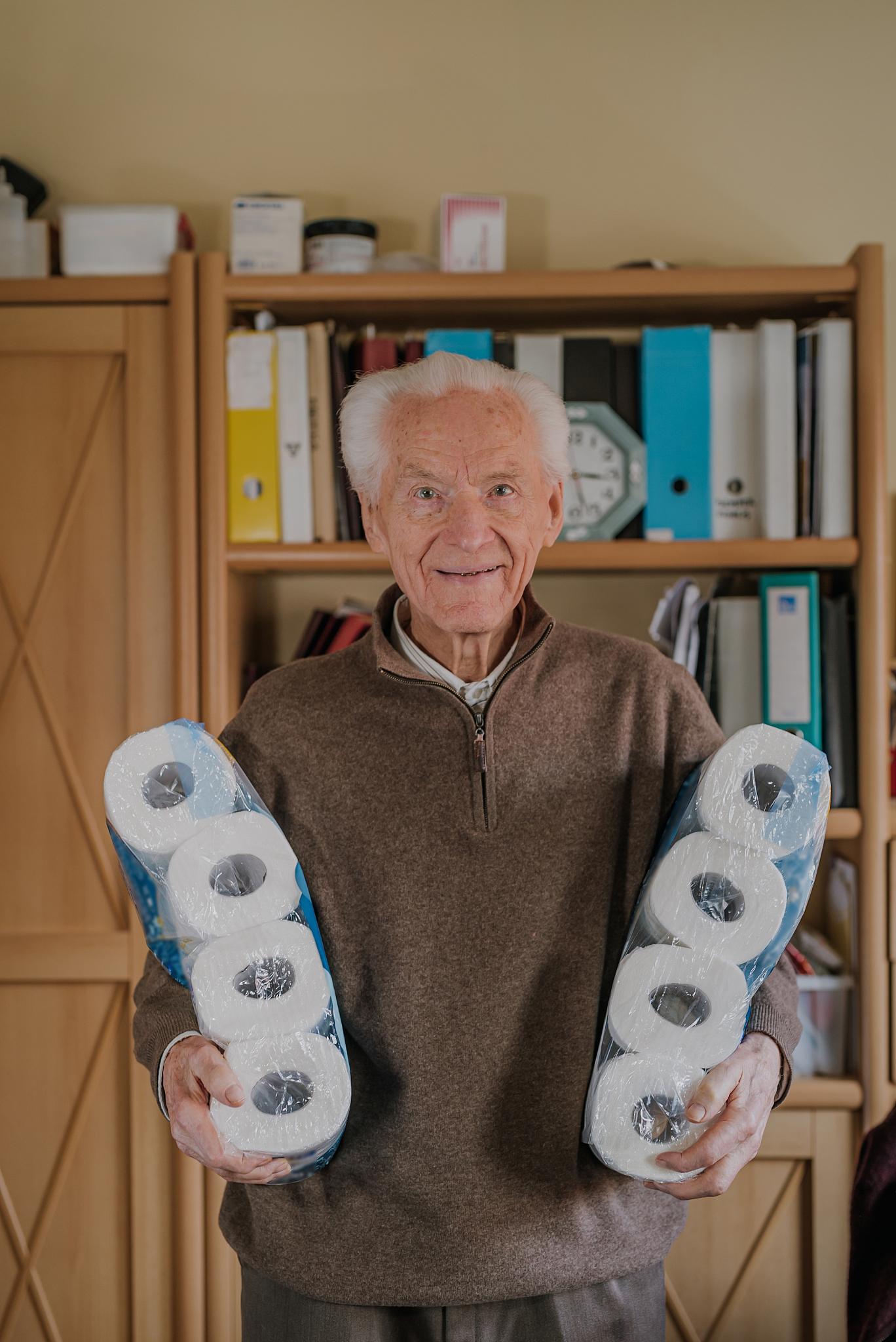 old man holding two packs of toilet paper