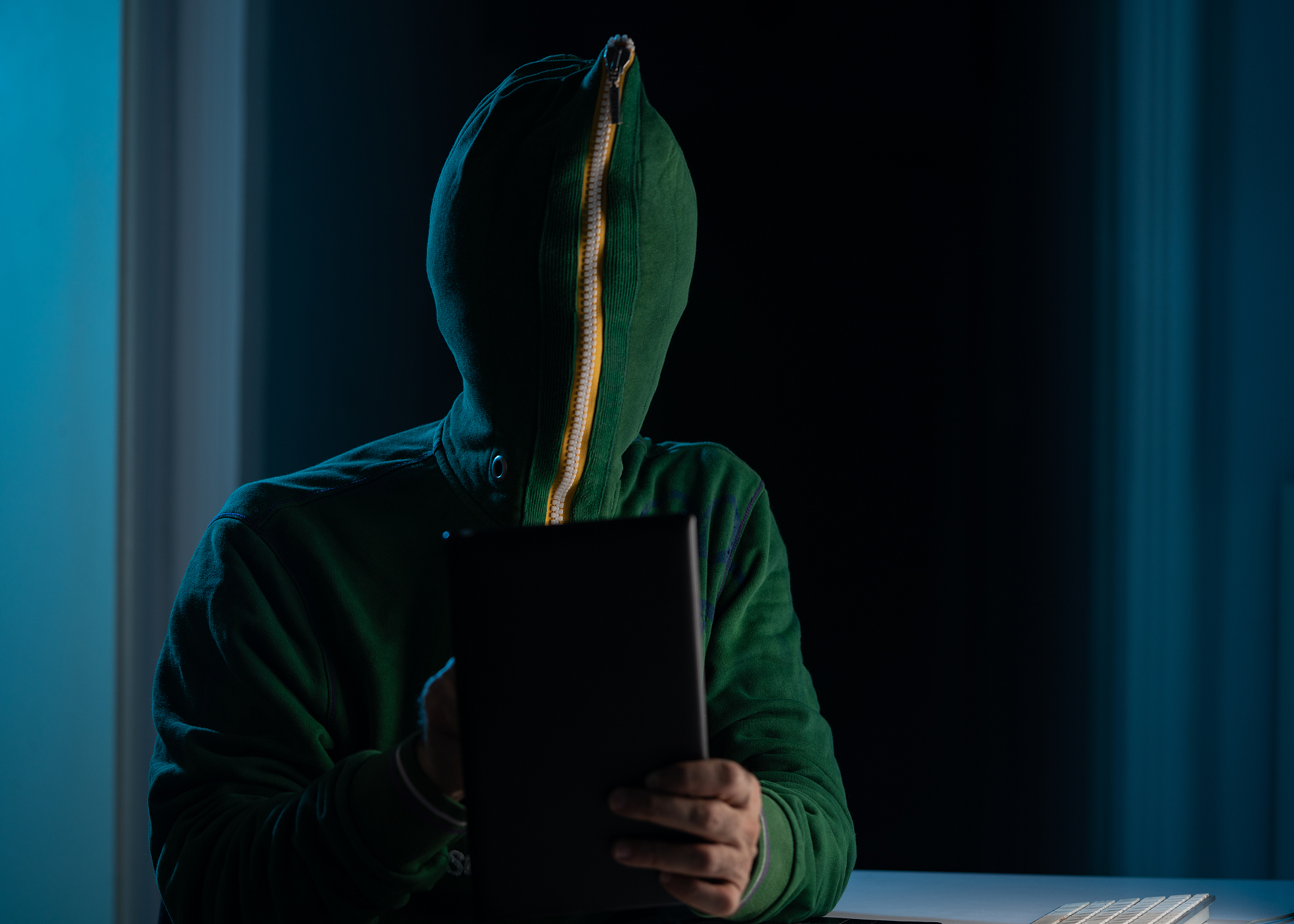man wearing zipped hooded shirt and mask using laptop in dark to