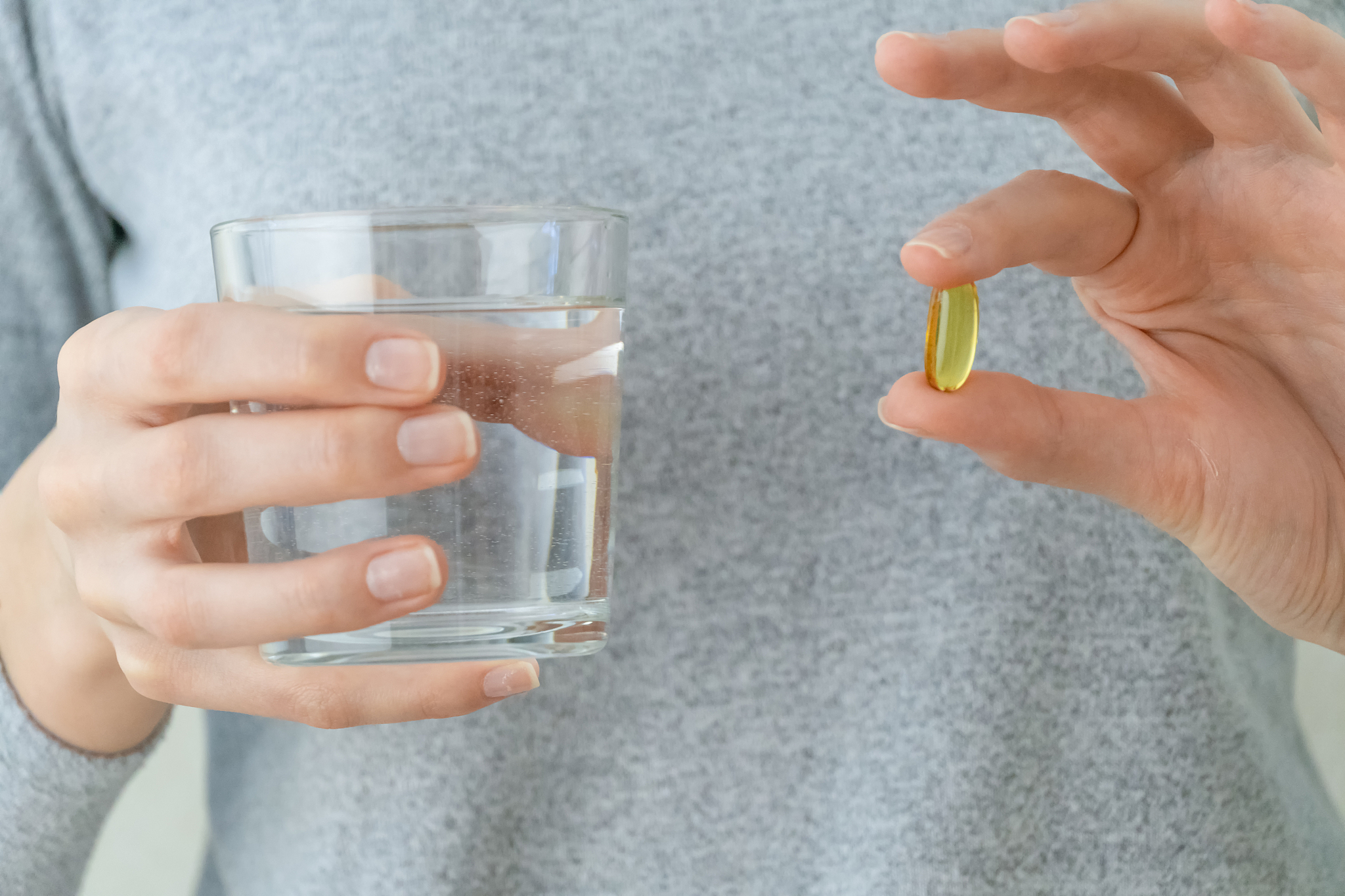 woman in a gray jacket is holding an omega-3 fish oil capsule an