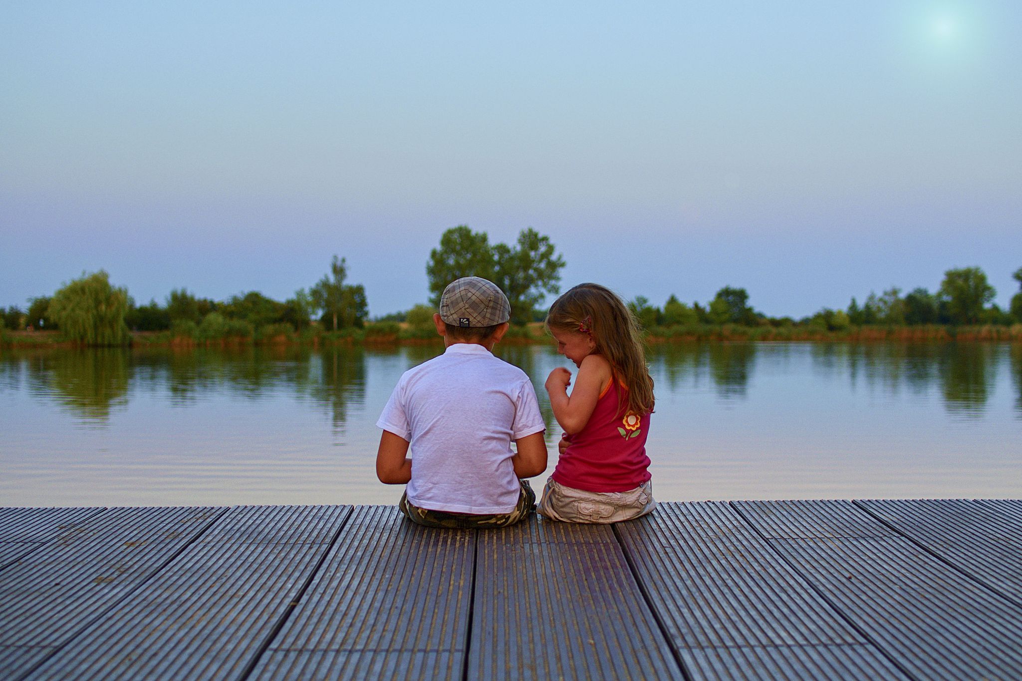 boy with flat cap and little girl are sitting on pier. love, fri