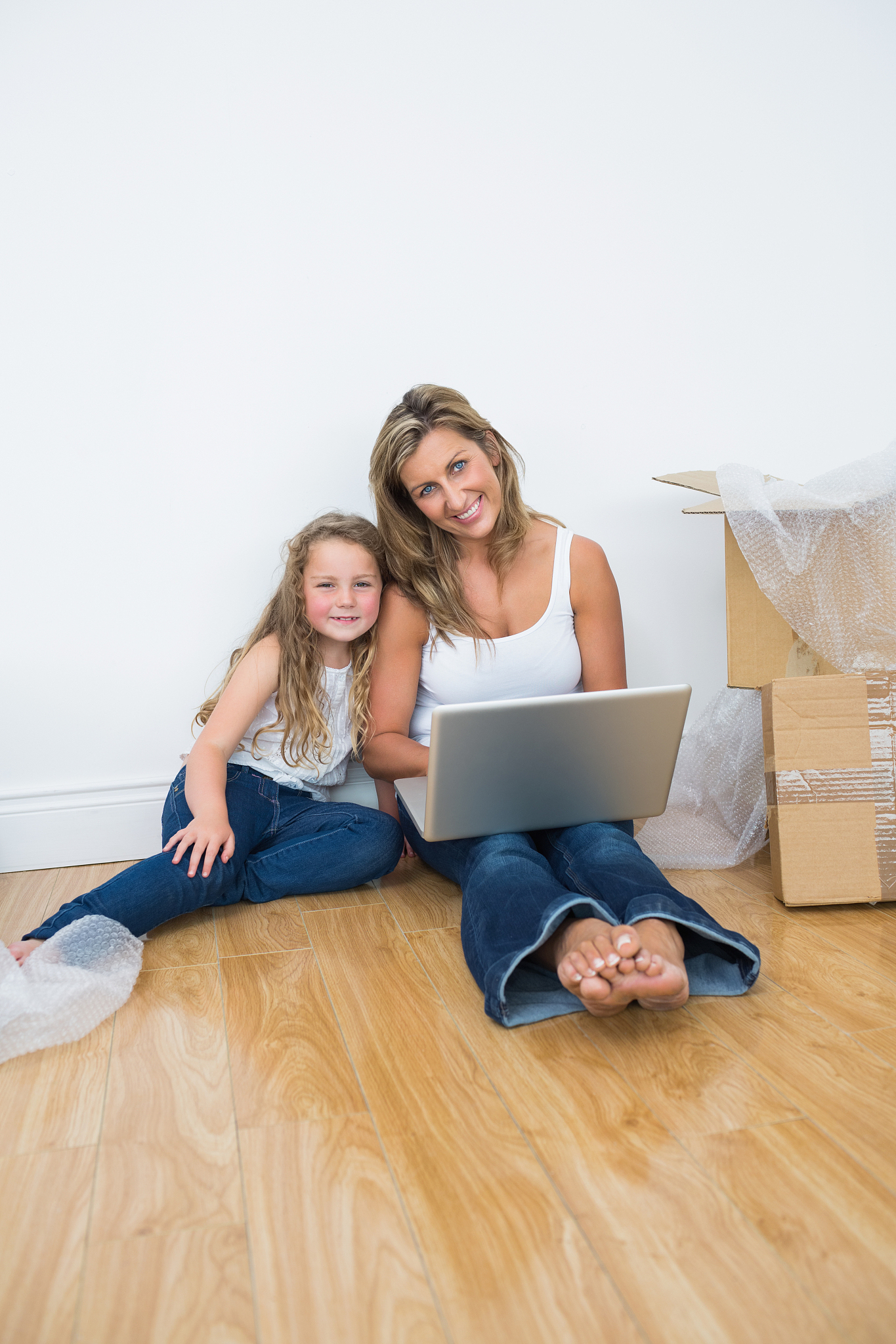 smiling daughter and mother sitting on the floor and using lapto