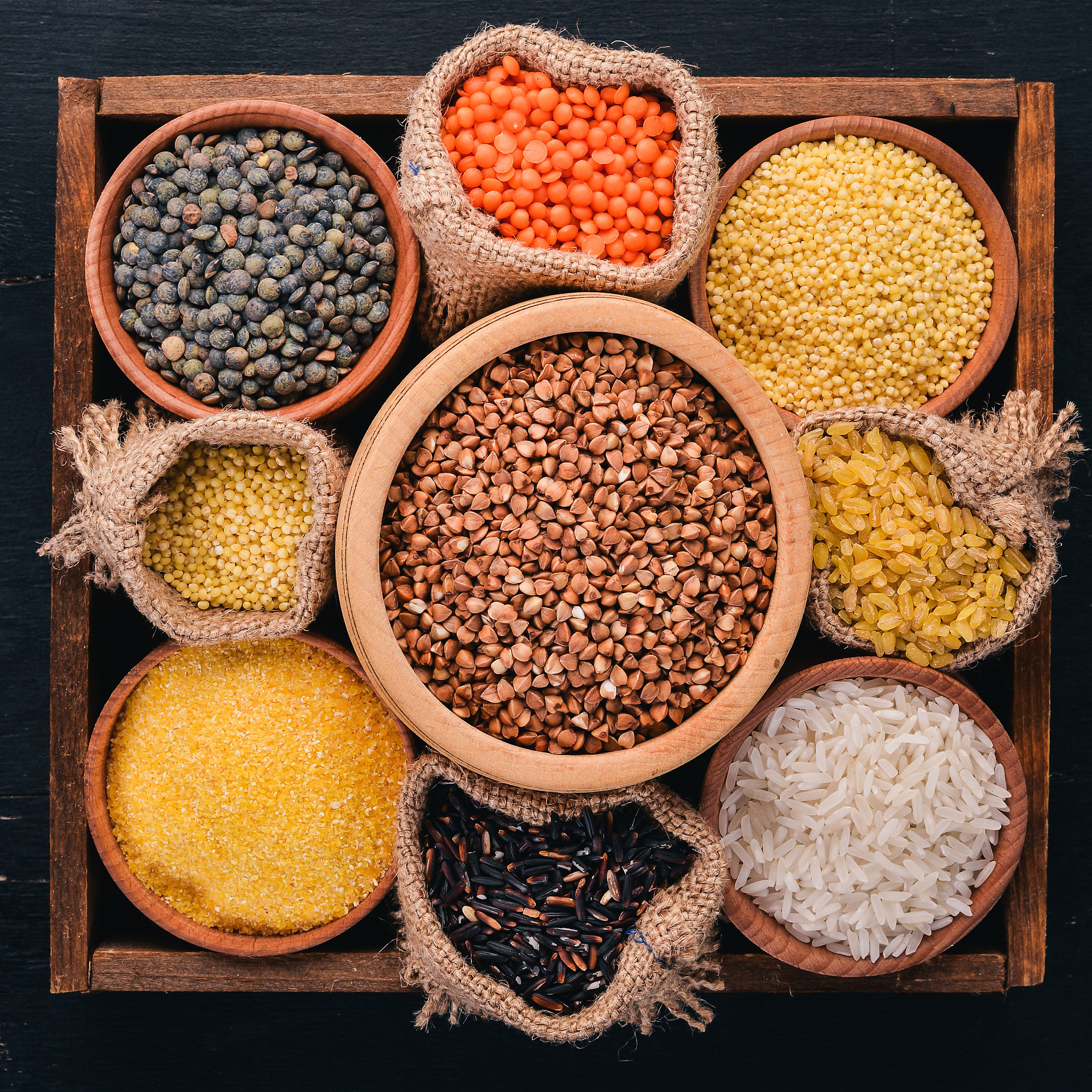 a set of cereals and grains in a wooden basket on a wooden backg