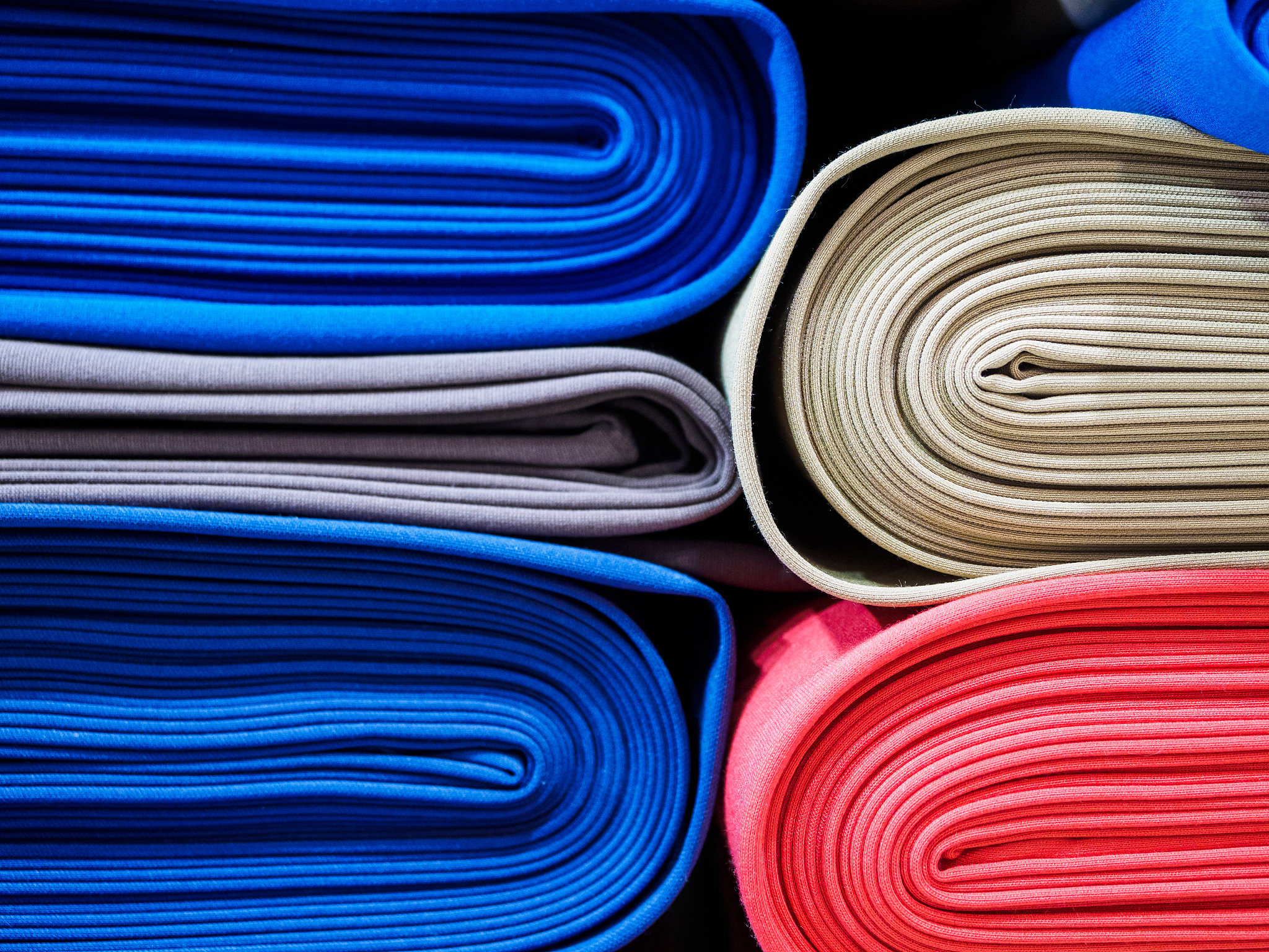 rolls of bright colored fabric are neatly stacked in a row on th