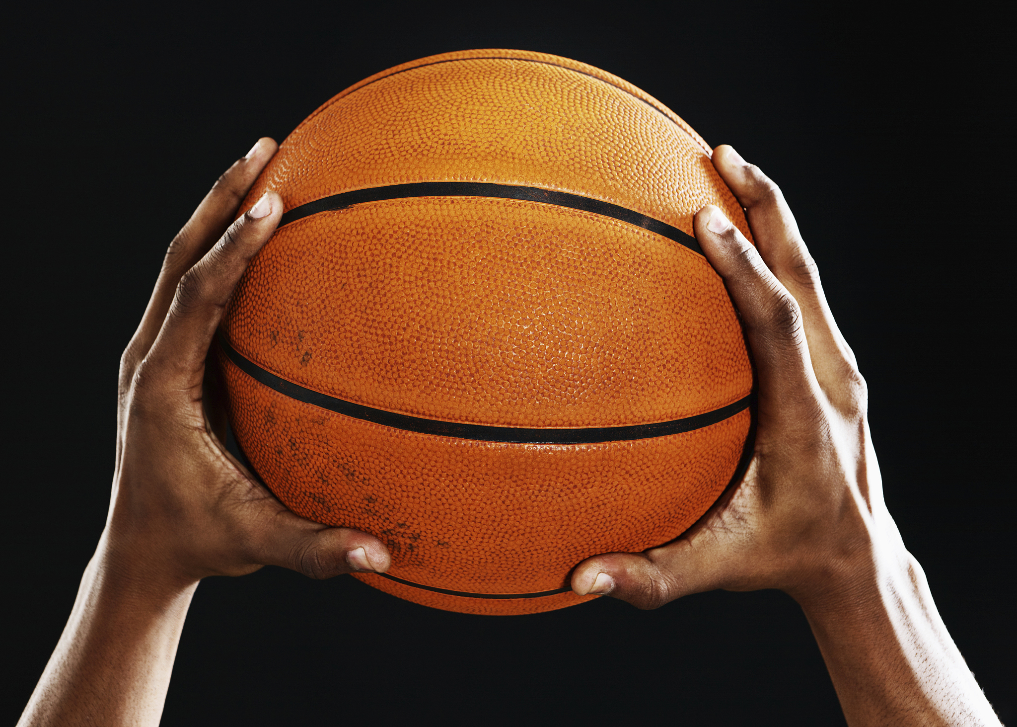 male hands hold up a basketball against black
