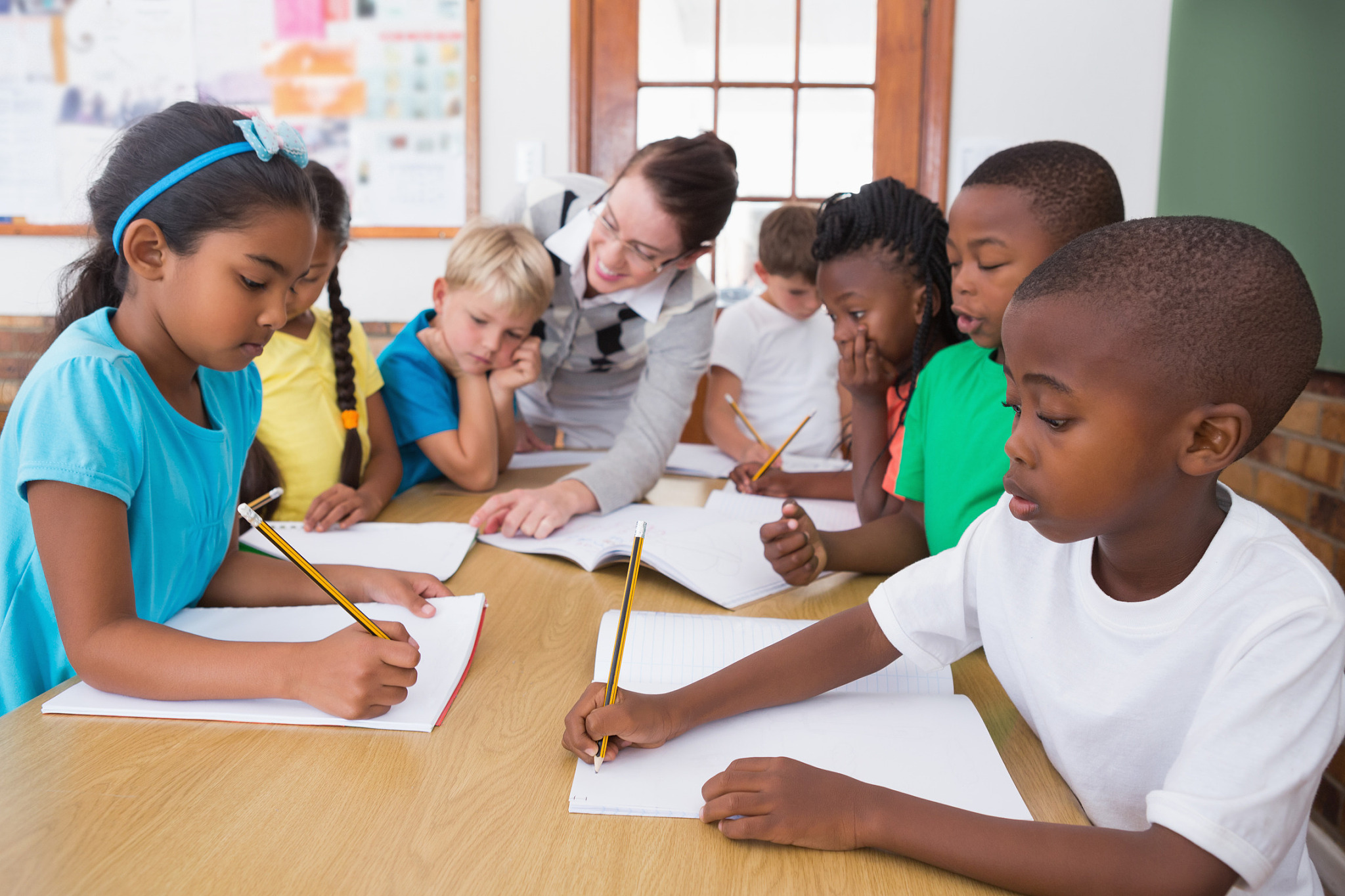 teacher and pupils working at desk together at the elementary sc