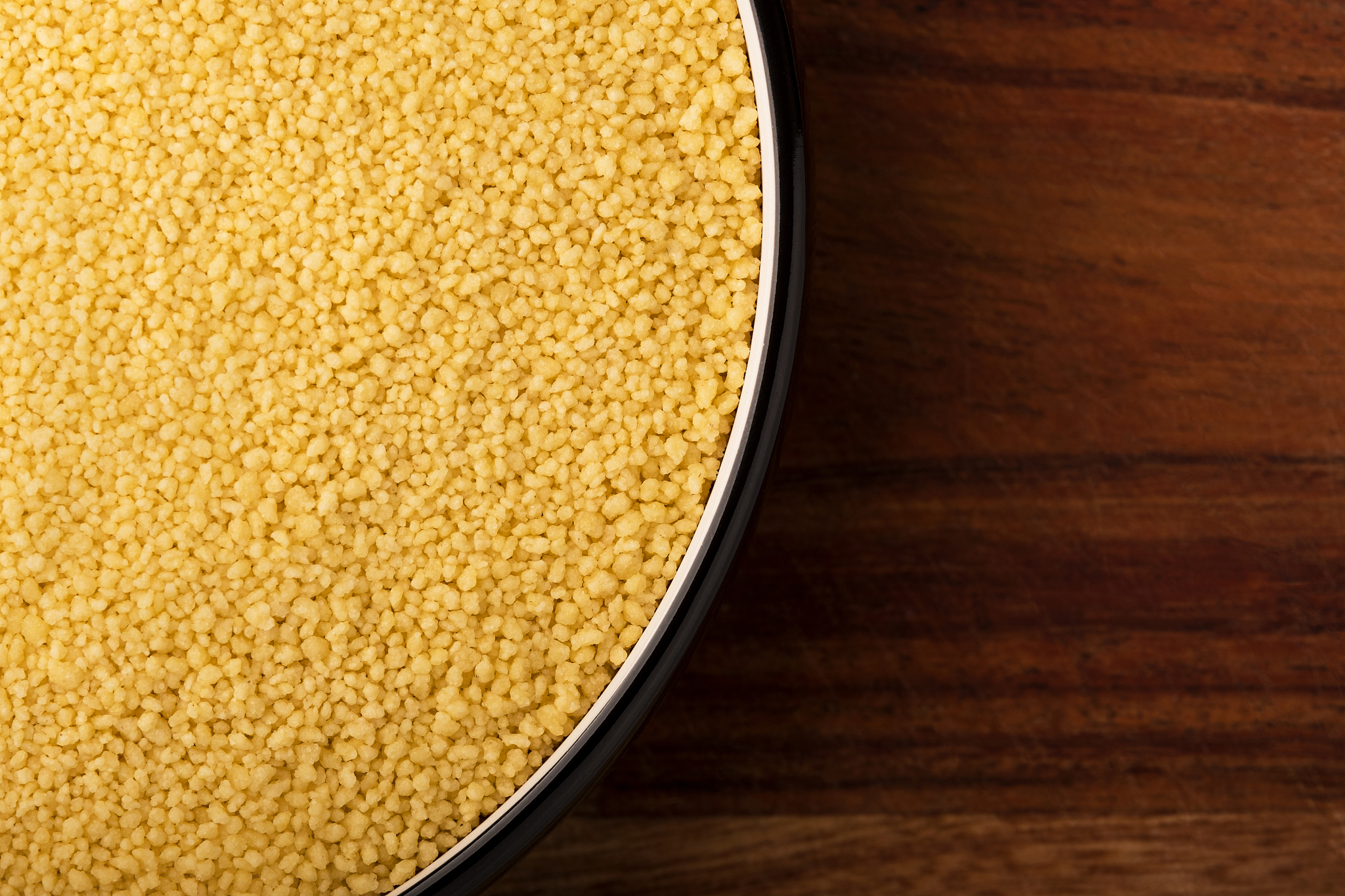 raw couscous in bowl on dark wooden background from above