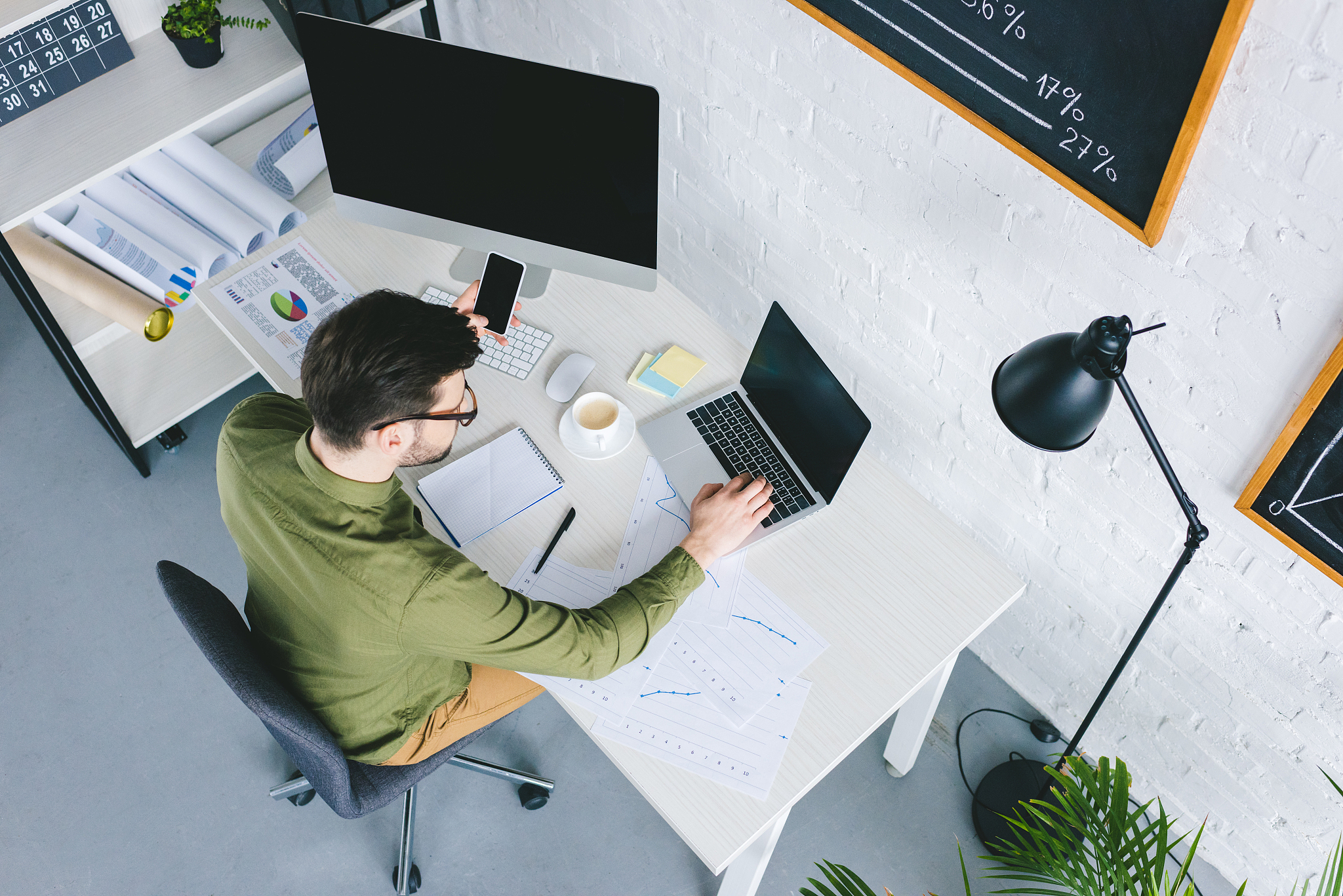 overhead view of young freelancer working by laptop and holding 
