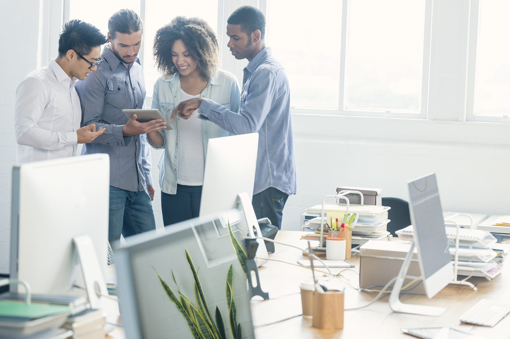 4 people working on a digital tablet in an office.