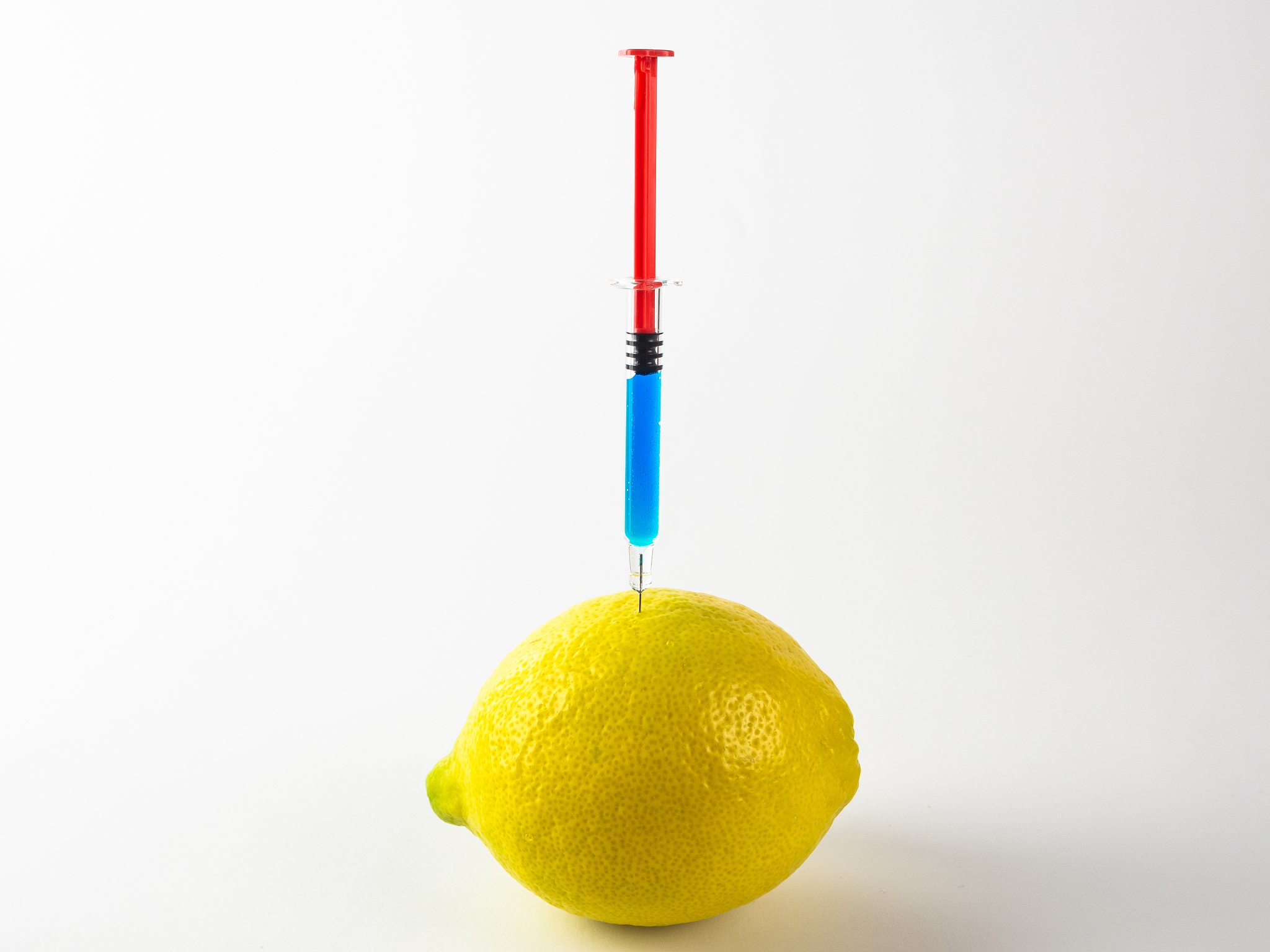 lemon with a syringe stuck with blue substance on white backgrou