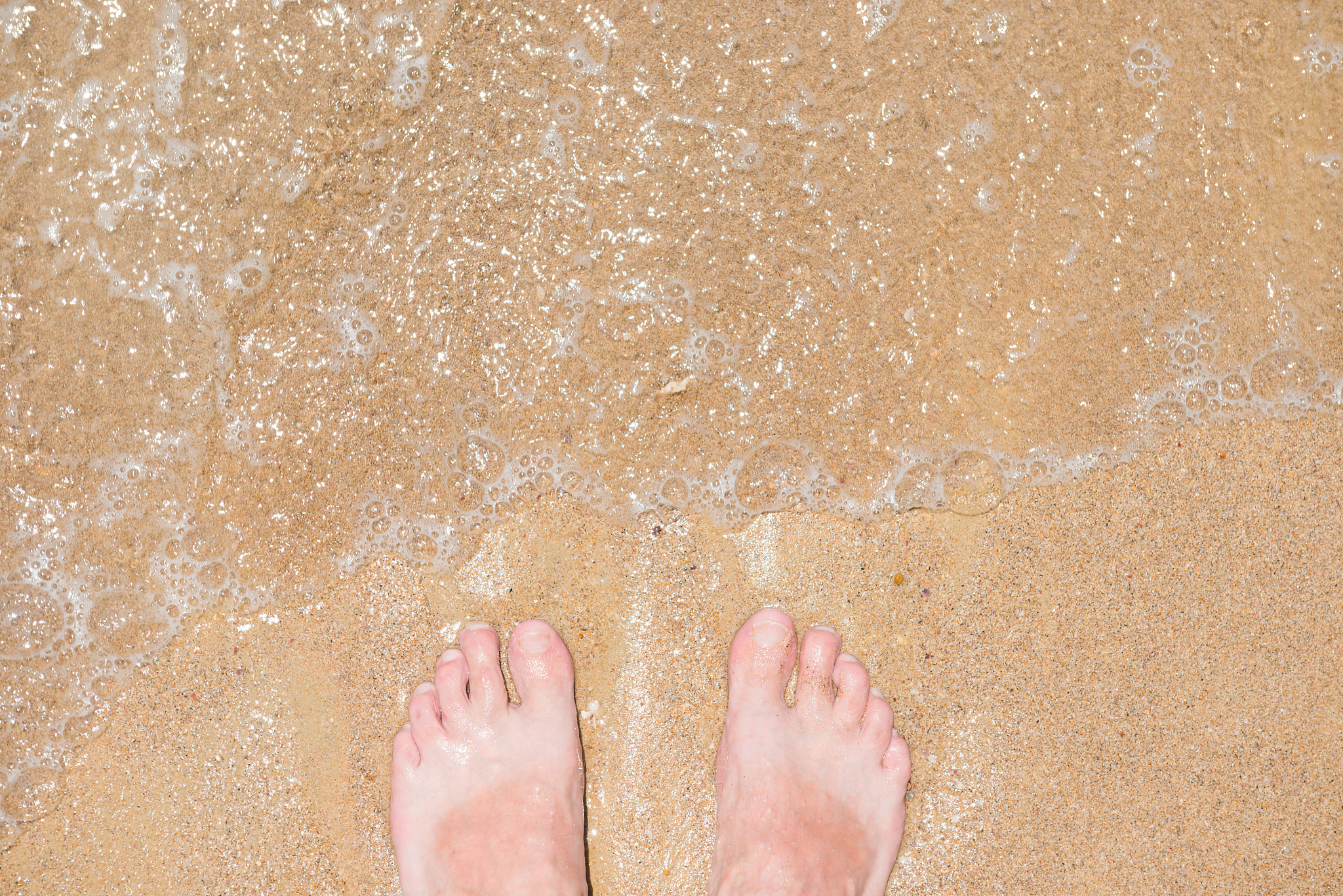 close up of bare human feet on sand by sea