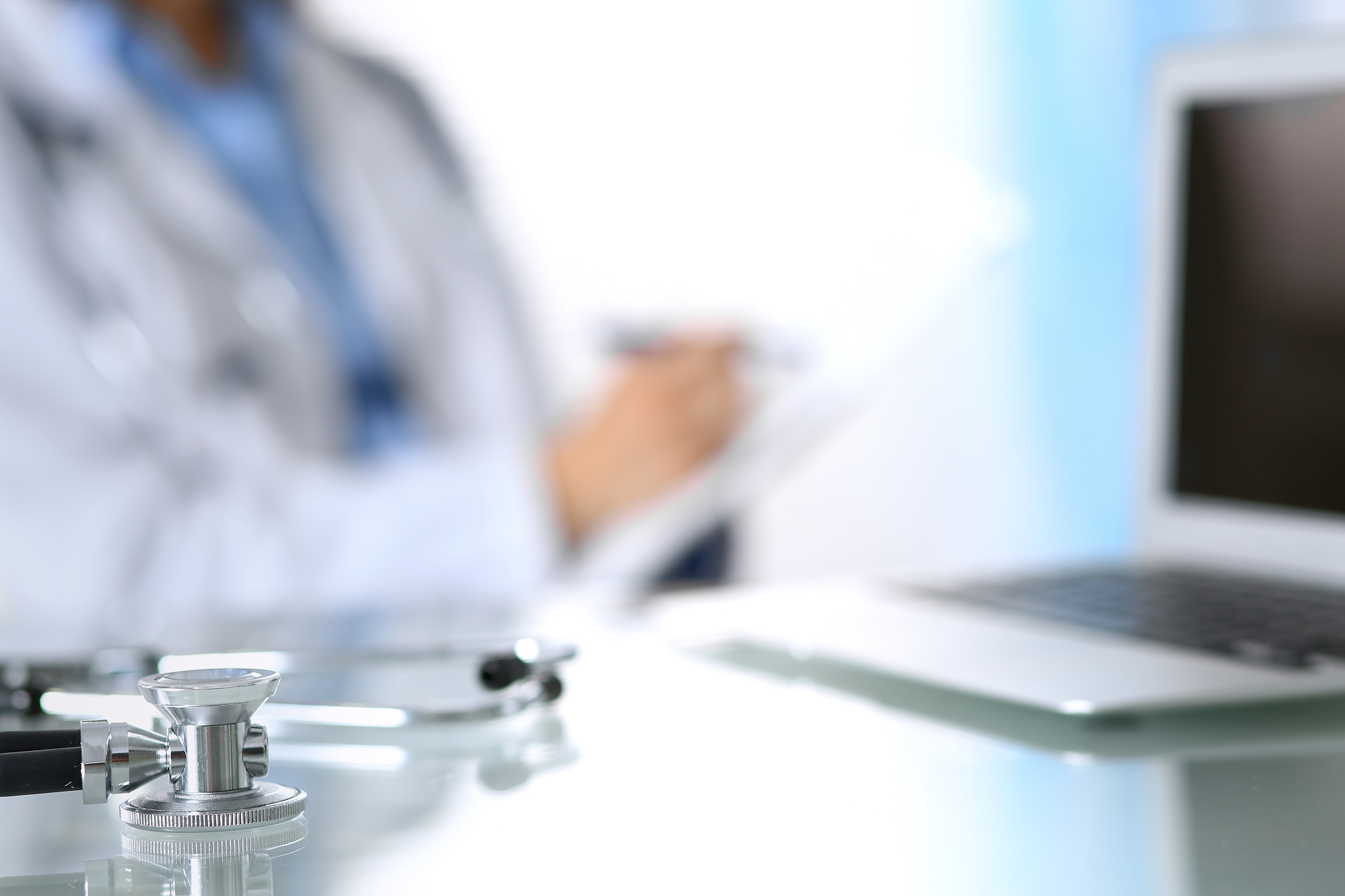 stethoscope lying on glass desk with laptop computer at busy phy