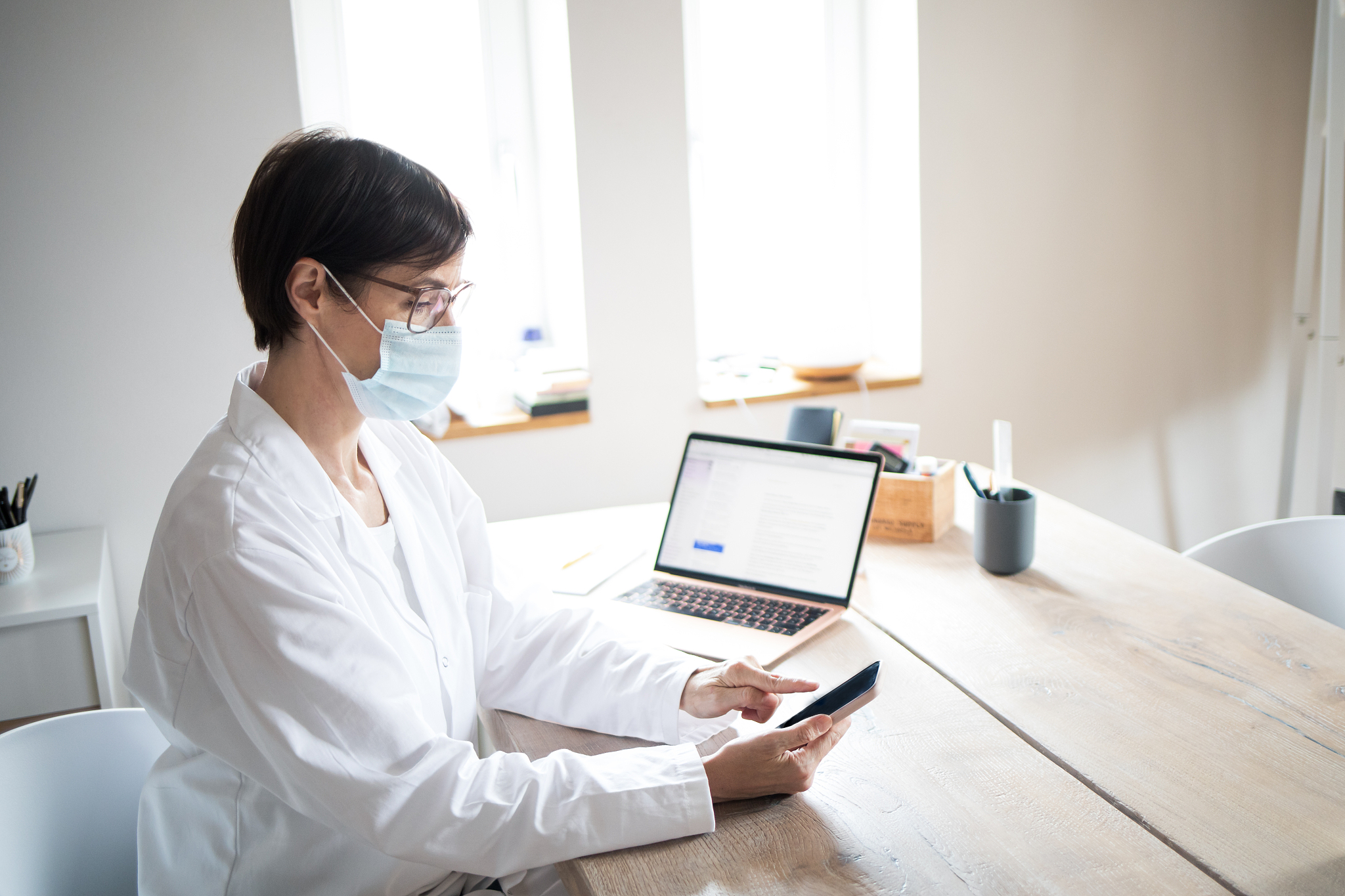 woman works in doctor's coat and mouthguard in the home office o